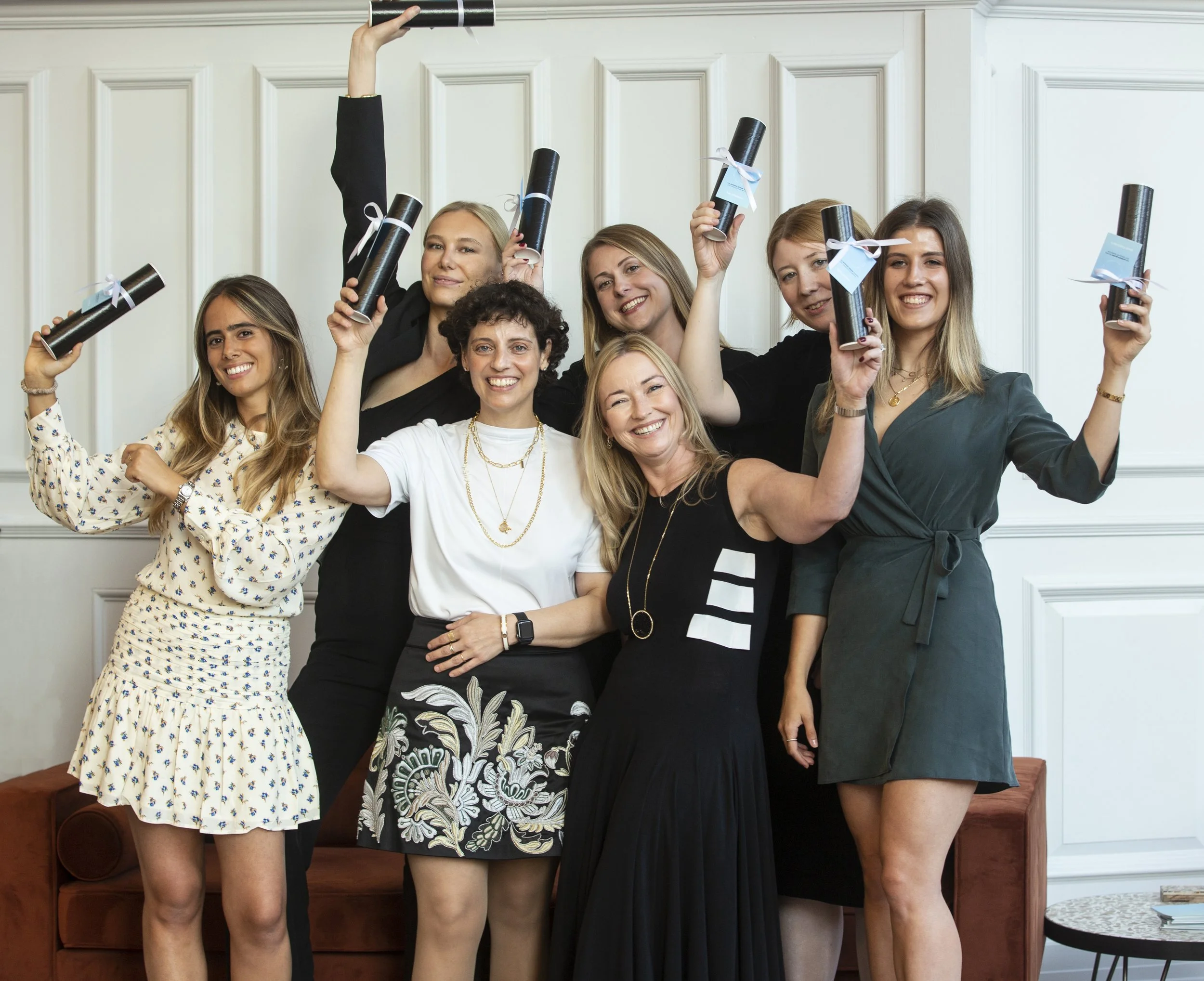 Group of women celebrating with diploma scrolls in a showroom.