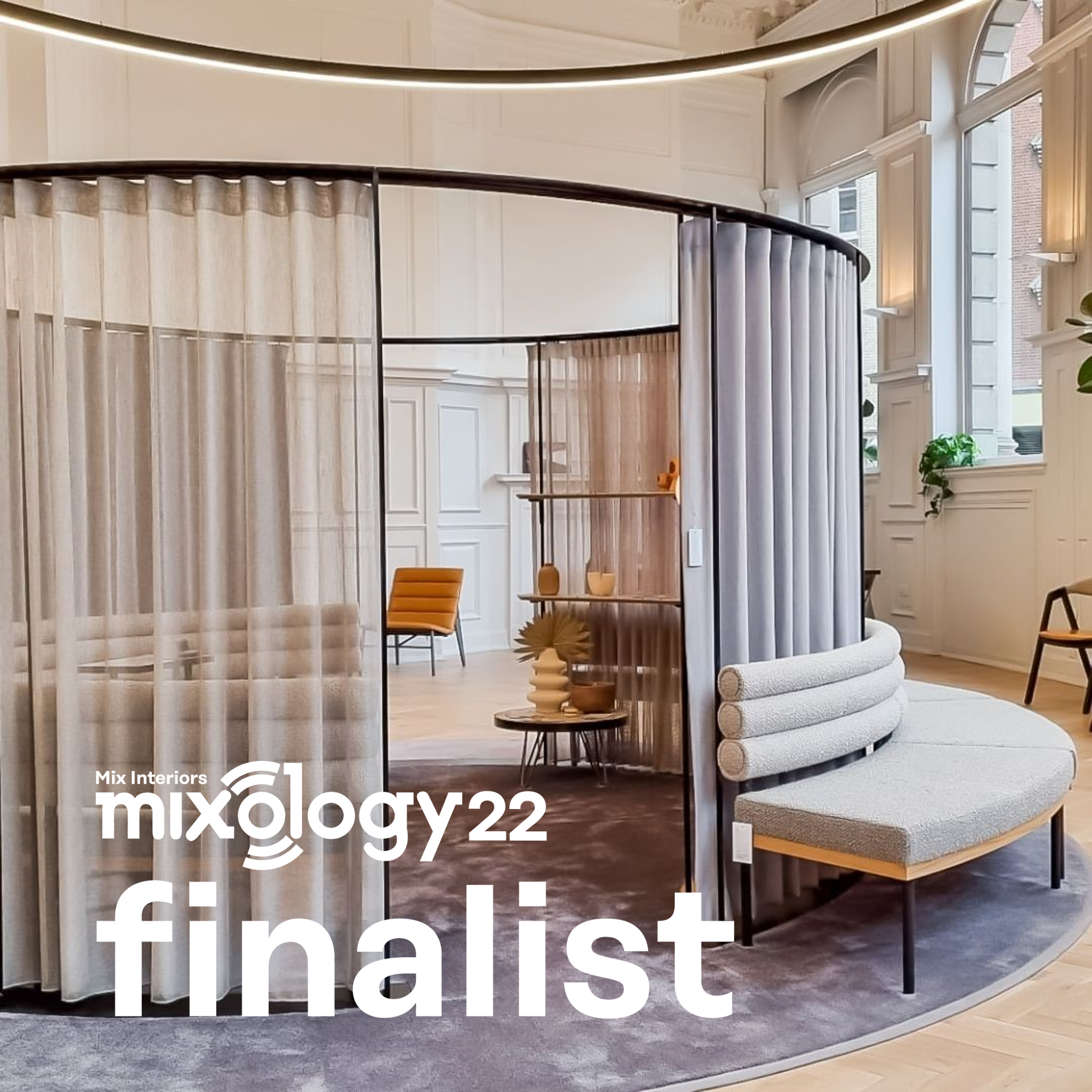 Interior of a modern, circular room with a semi-private area divided by sheer curtains, featuring a curved upholstered seating bench and shelves with decorative items; natural light coming through large windows.