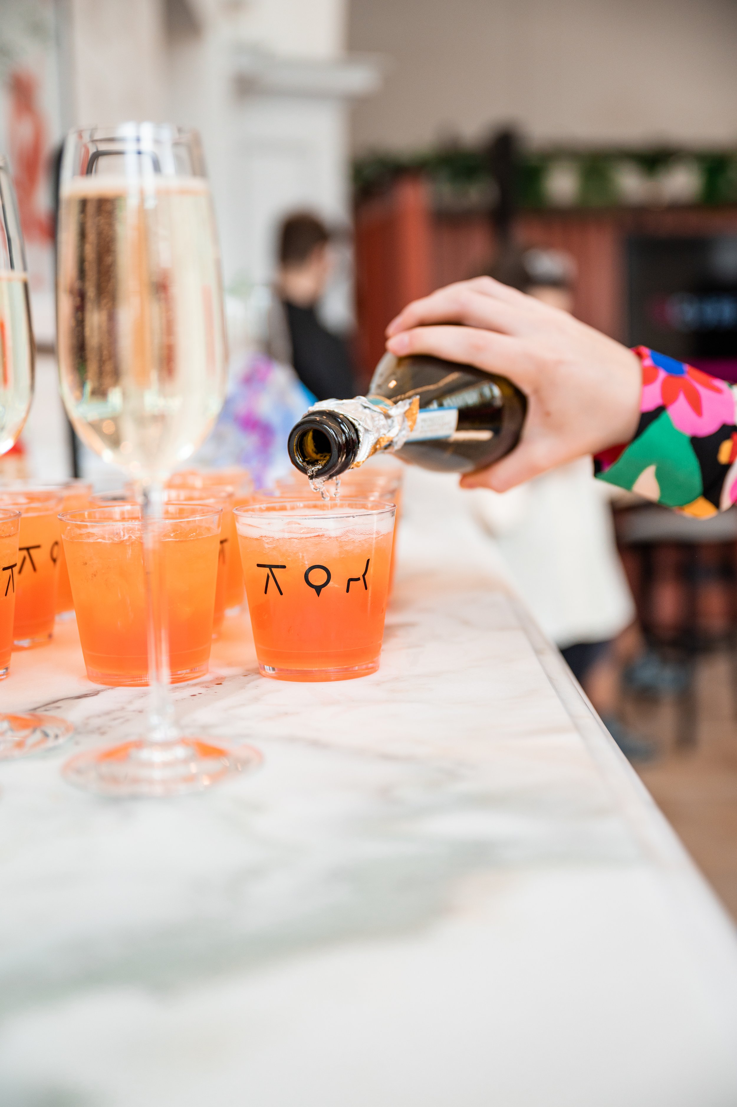 Person pouring champagne into pink cocktails with smiley face and moon symbols at a party or celebration event.