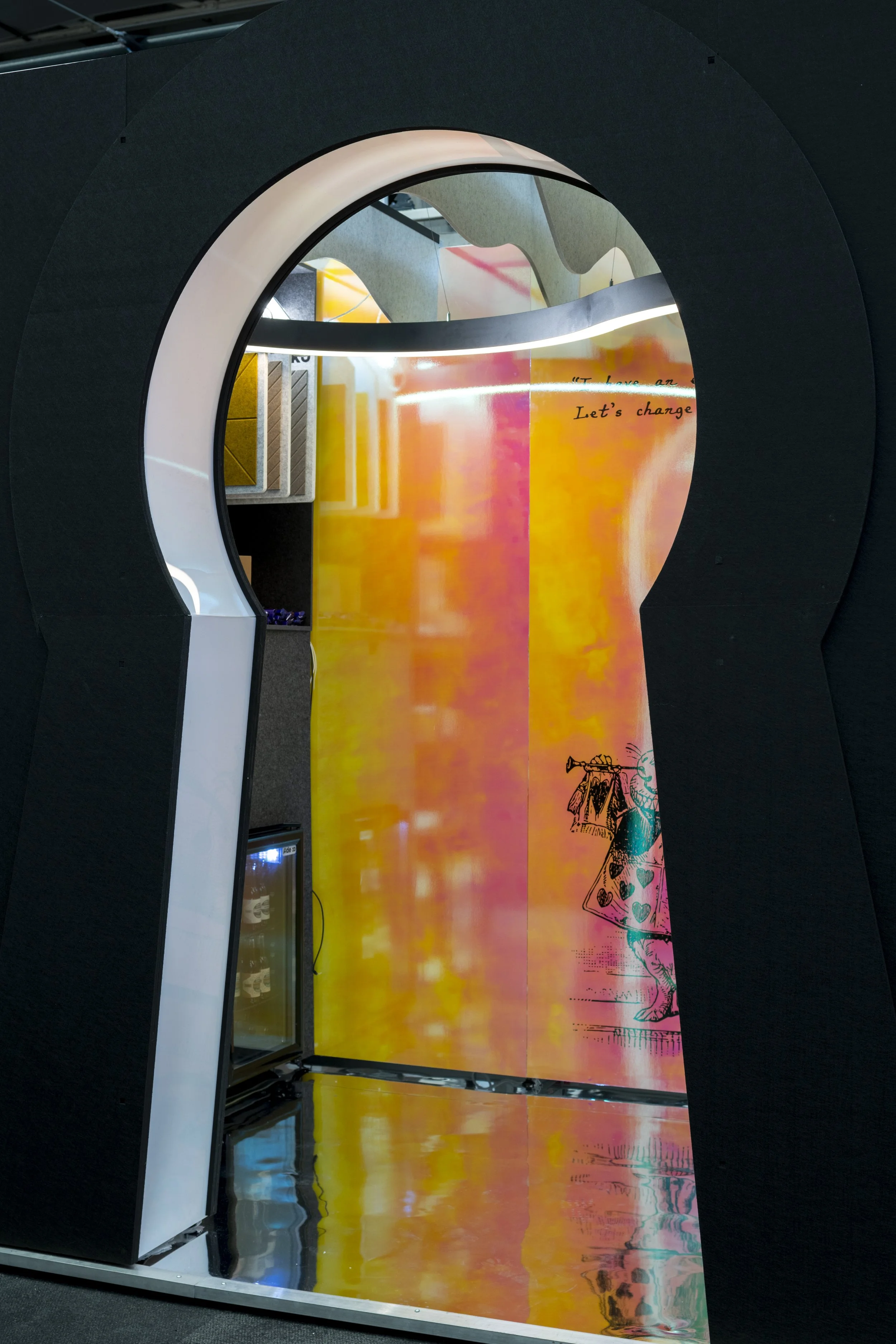 View through a large black keyhole-shaped frame revealing a colourful background with a mixture of orange, yellow, and pink hues, and partial illustrations of Alice in Wonderland scenes.