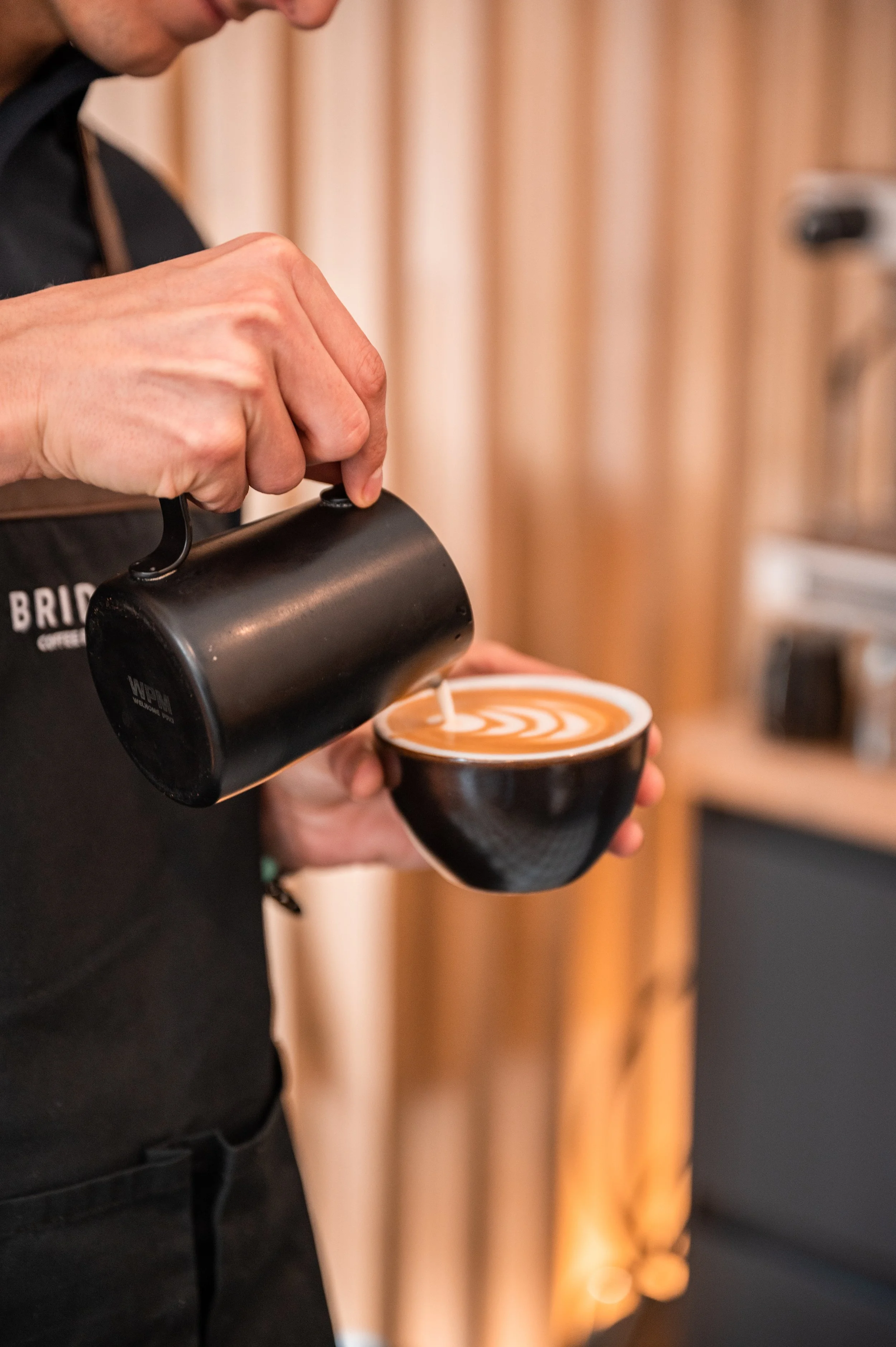 Barista pouring steamed milk into a cup of coffee with latte art.