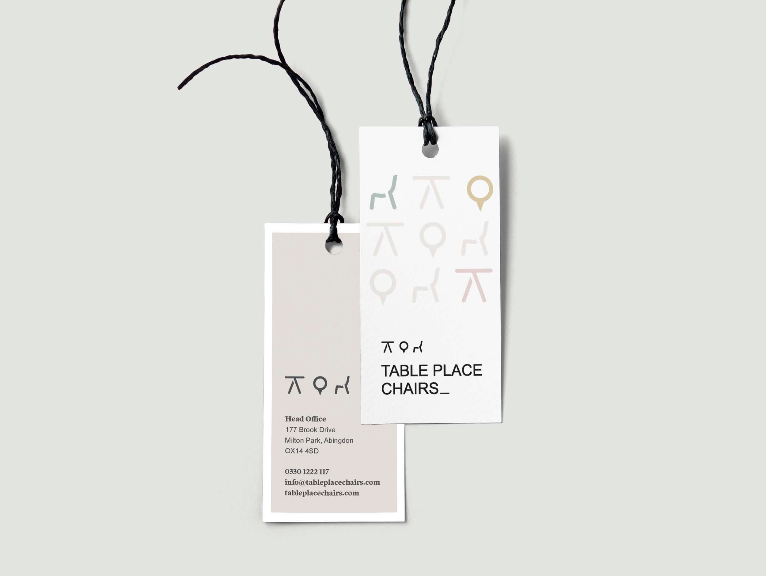 Two business cards hanging by black strings against a light gray background. The front card features minimalist chair and table icons with the text 'TABLE PLACE CHAIRS_'. The back card provides contact information for a business 