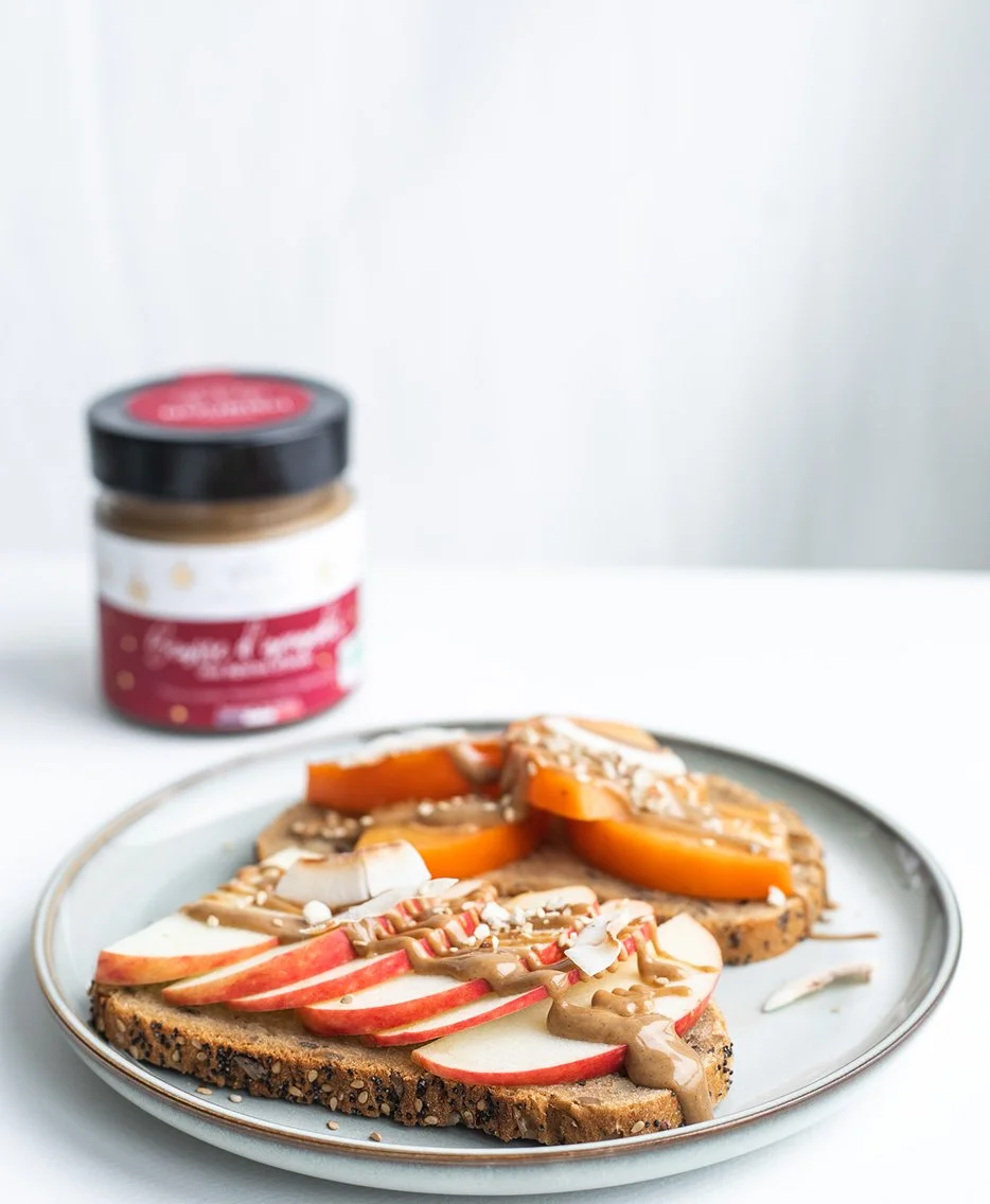 Assiette de tartines garnies de fruits, avec un pot de pâte à tartiner végétale en arrière-plan — photographie culinaire pour communication visuelle authentique.