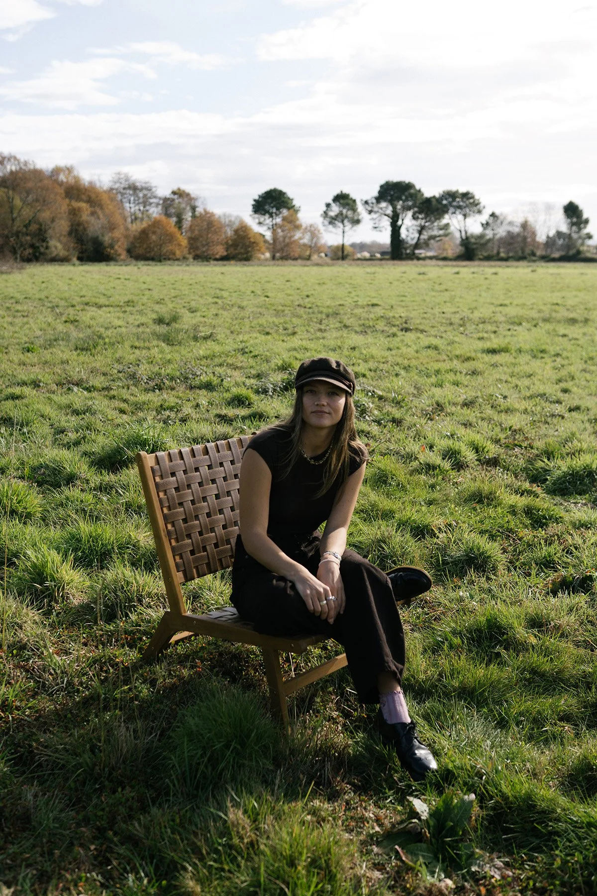 Portrait en extérieur d’une femme assise dans un champ, vêtue de noir, sous un ciel nuageux — image évoquant la connexion à la nature et la contemplation.
