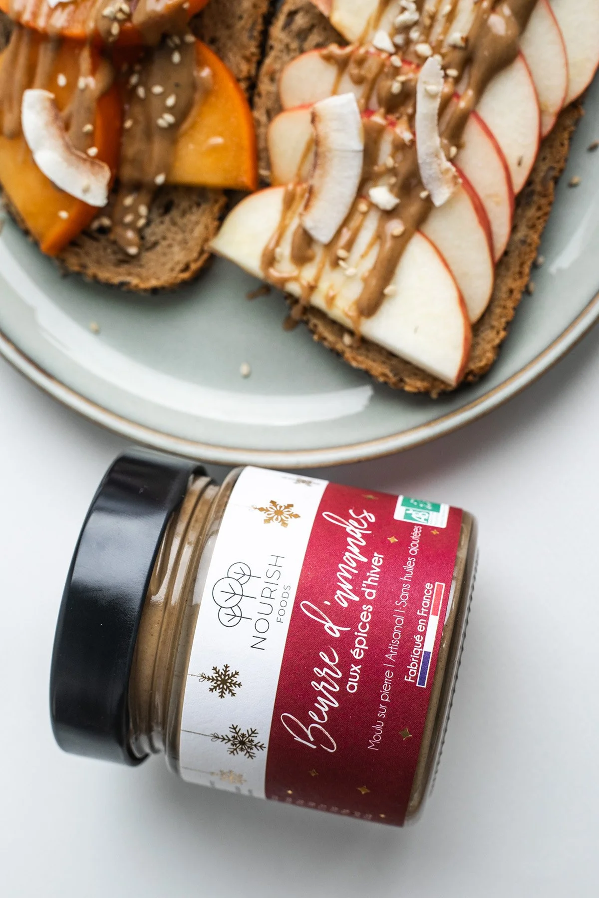 Photographie culinaire d’une tartine garnie de pommes, poires et pâte à tartiner hivernale, avec pot de marque visible — projet de stylisme food et packaging.