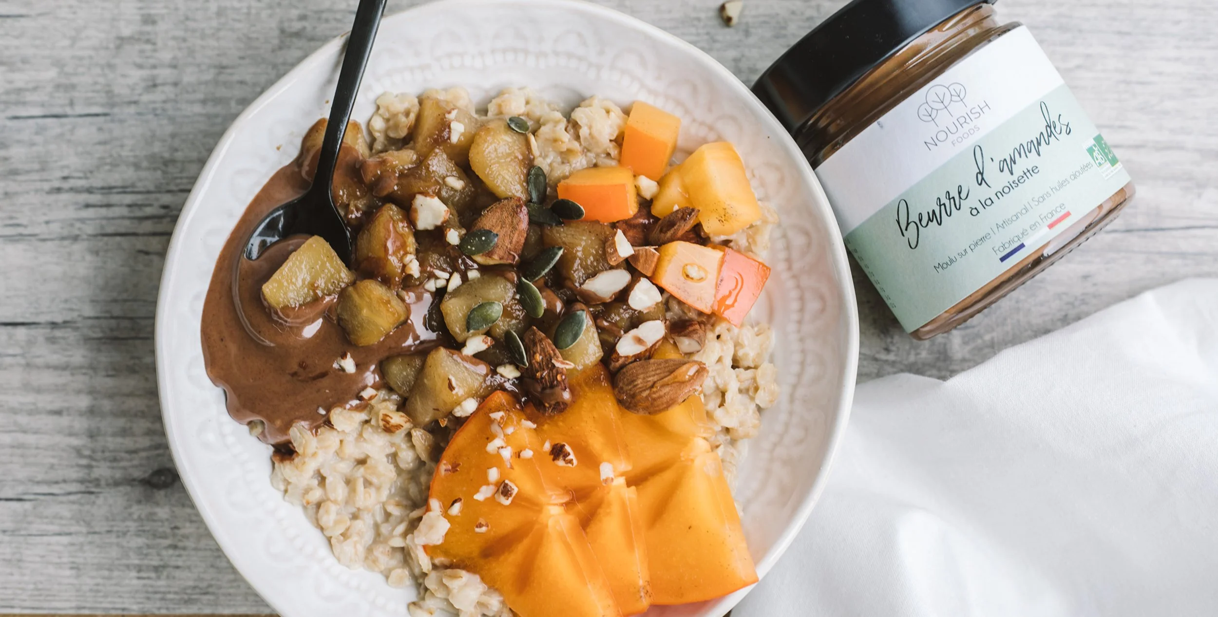 Bol de porridge avec compote de potiron, noix et graines, à côté d’un pot de beurre d’amande — photo produit bien-être pour boutique naturelle.