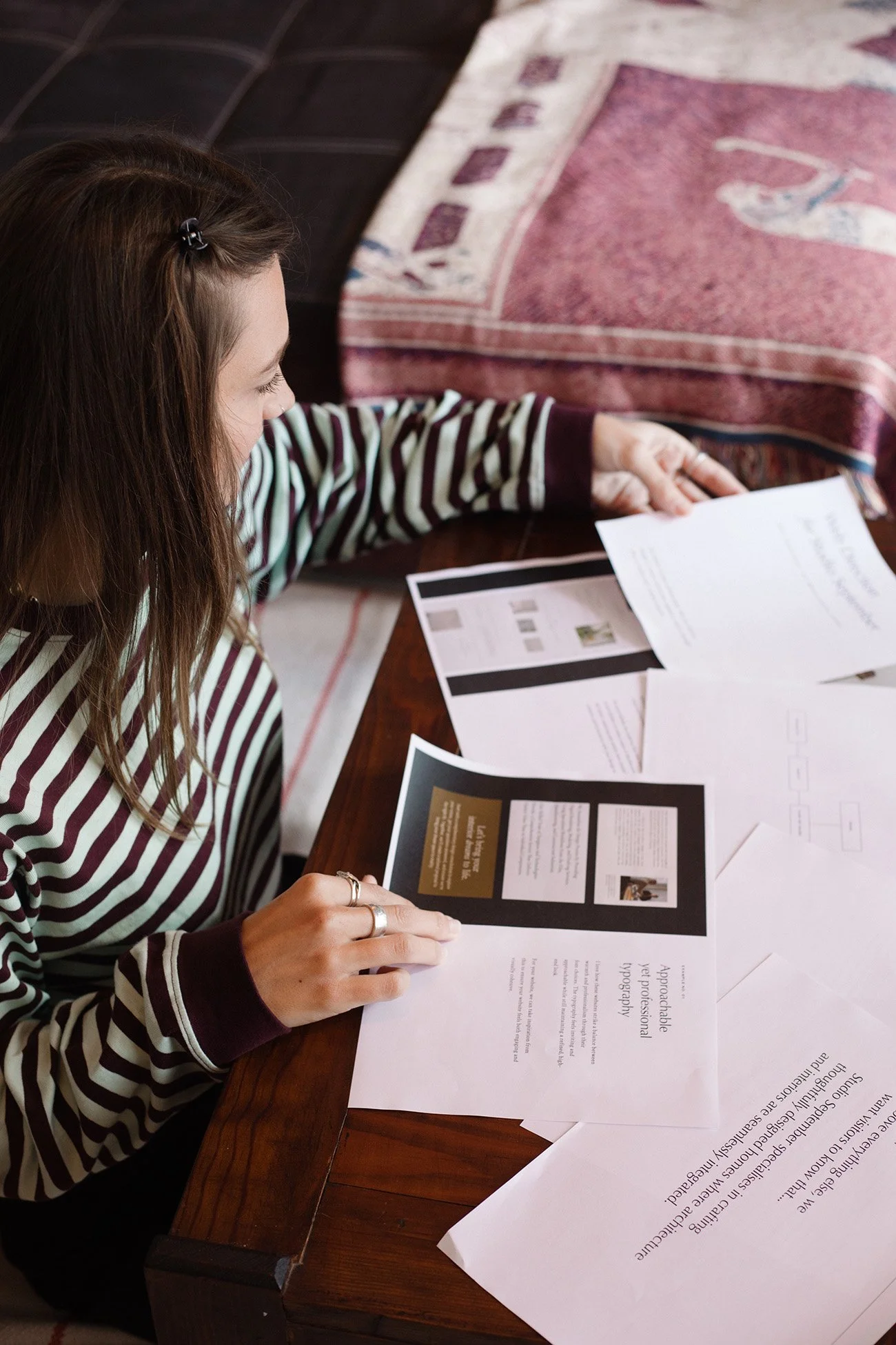 Femme lisant des documents sur une table en bois, entourée de brochures — image de branding créatif pour studio de design graphique.