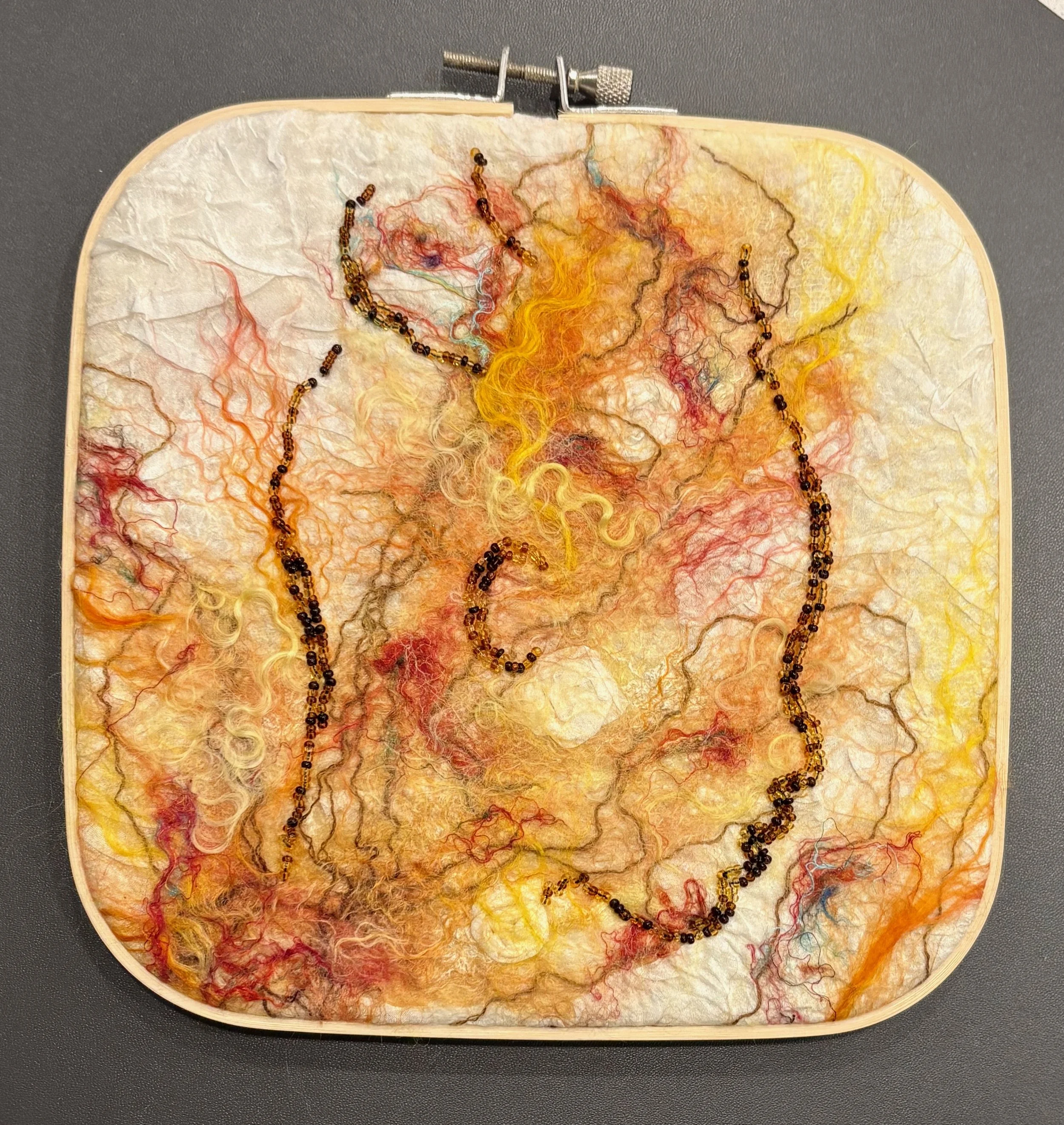 Embroidery hoop with a textile art piece featuring multicolored wool threads and beads outlining a woman's profile.