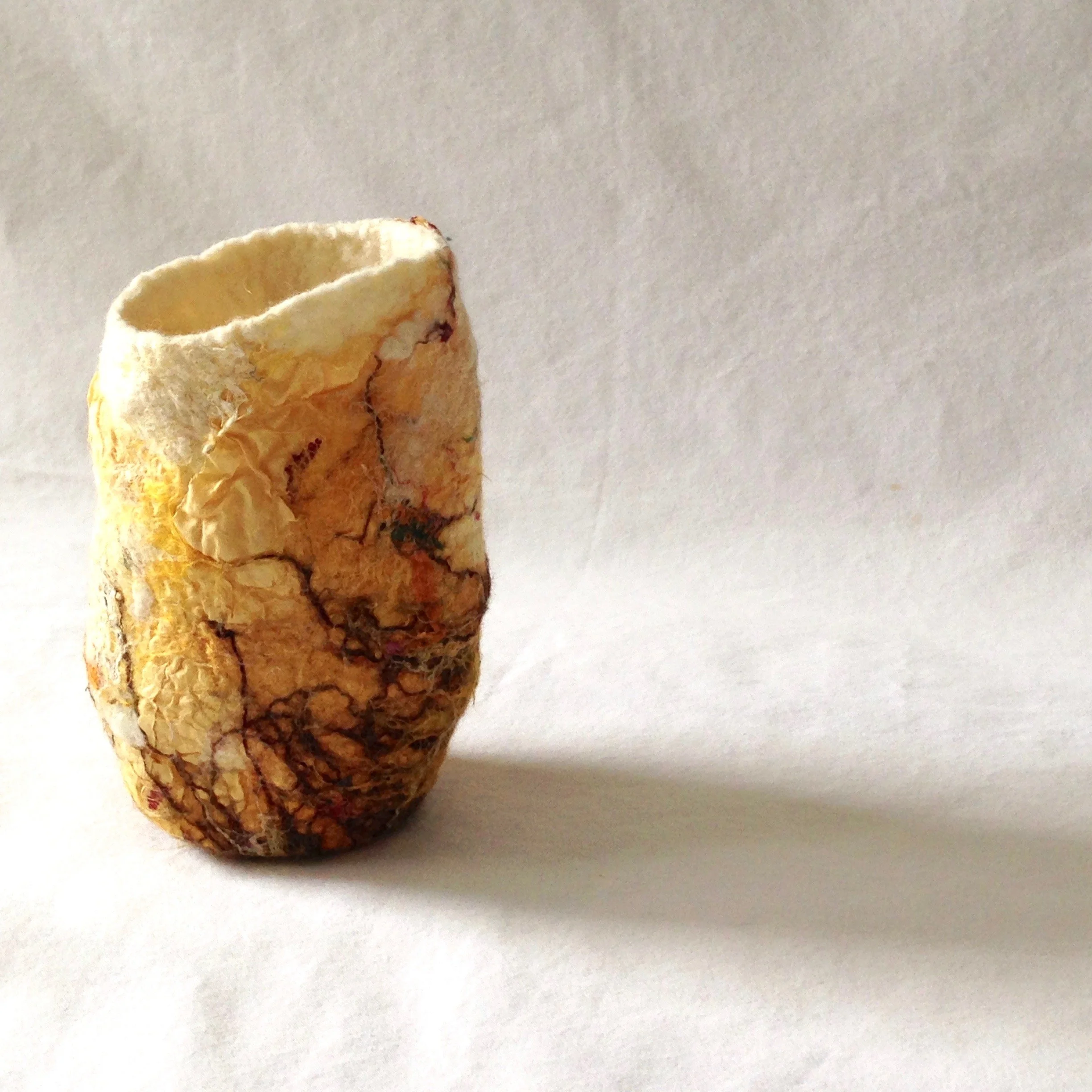 A handcrafted and asymmetrical felt vessel against a white background.