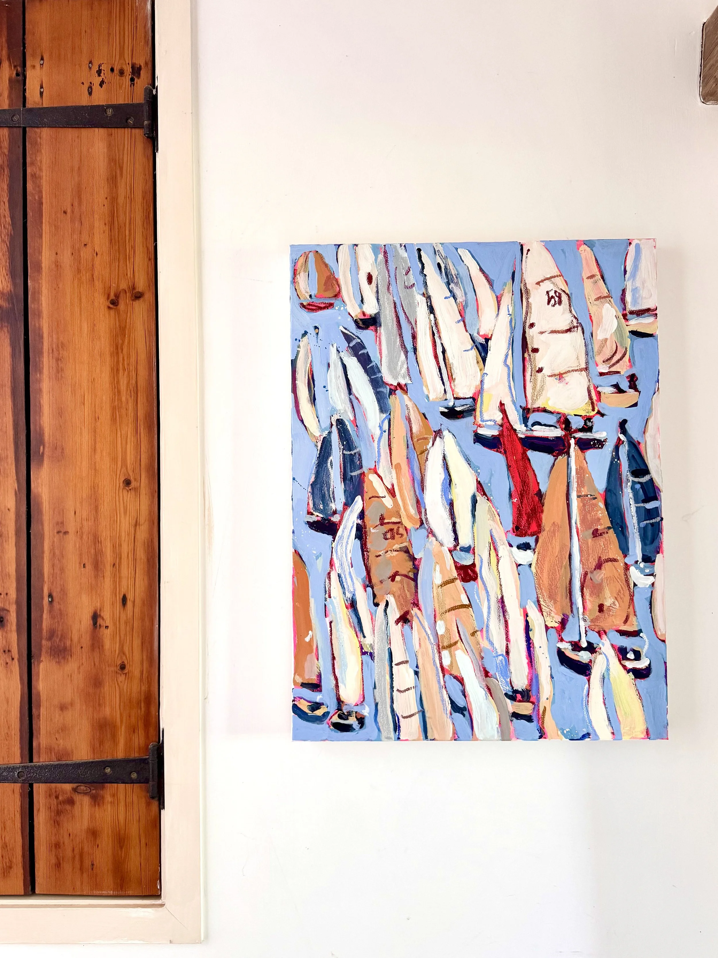 An abstract painting with colorful vertical brushstrokes on a blue background, hung on a white wall next to a wooden door.