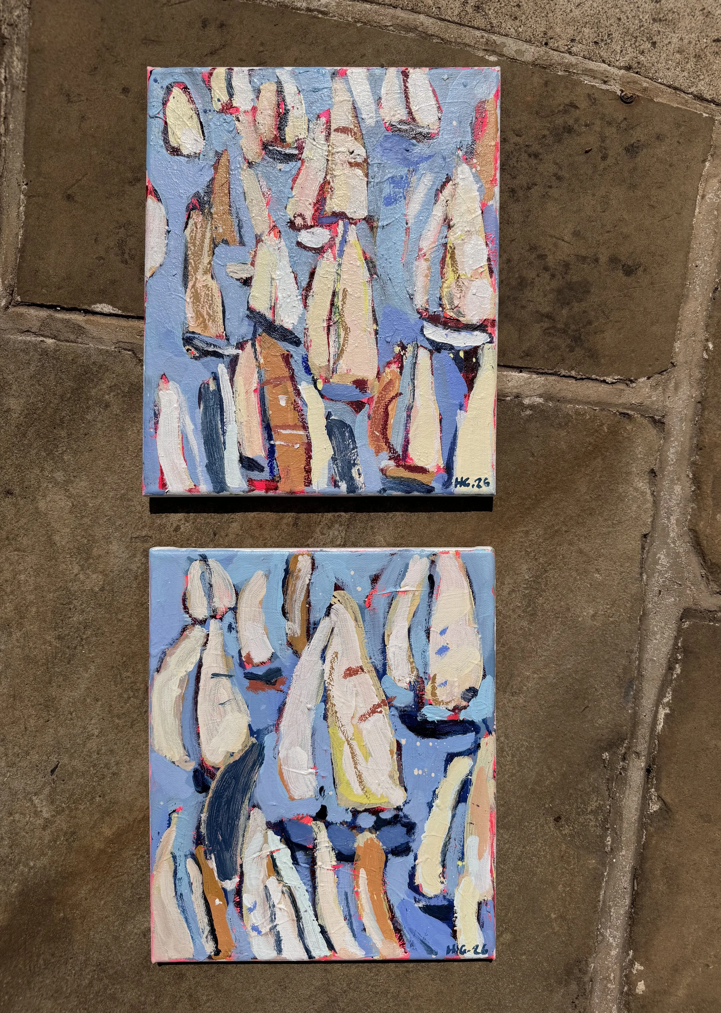 Two small abstract paintings with thick, expressive brushstrokes on a brick surface. The paintings feature a mix of light and dark colors, including blue, beige, and black, with hints of red and yellow. Signed with initials and dated 2026.