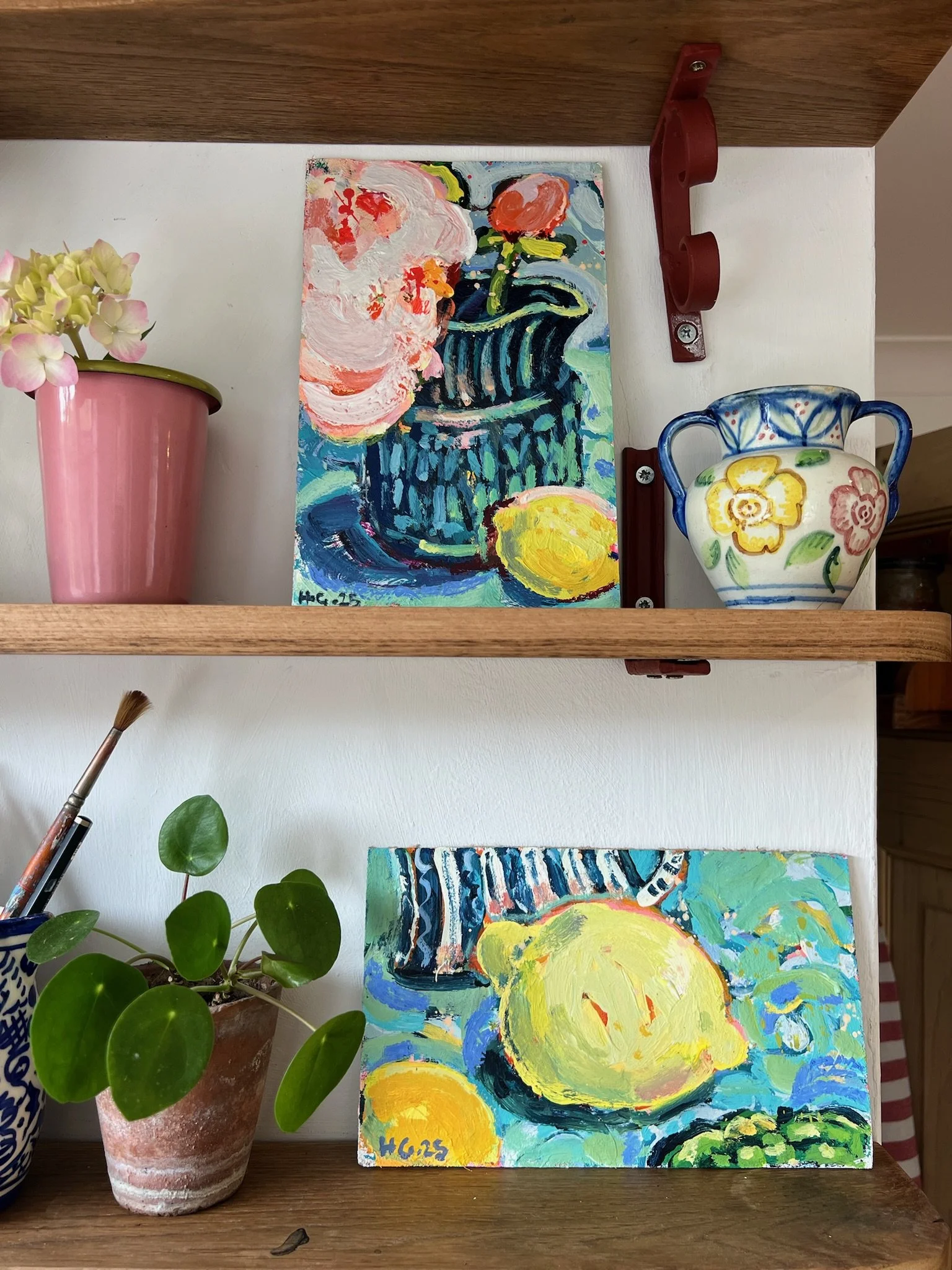 A still life painting inspired by Van Gogh's sunflower painting style, placed on a wooden shelf next to a pink flowerpot with hydrangeas and a colorful ceramic vase with flowers, on a white background.