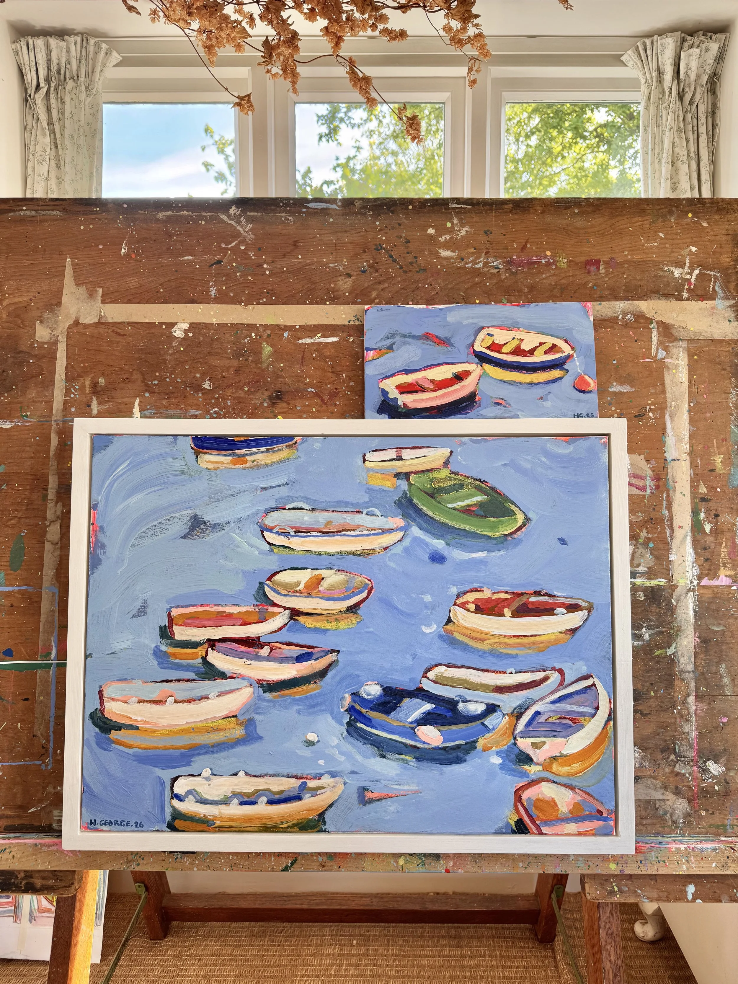 An artist's painting of lily pads on water, painted with bold brushstrokes and vibrant colors, on a canvas in front of a window with curtains and trees outside.
