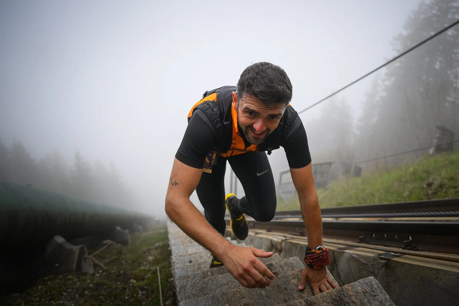 A man dressed in athletic gear climbing a set of stone stairs outdoors on a foggy day, with a backpack, on a mountain trail.