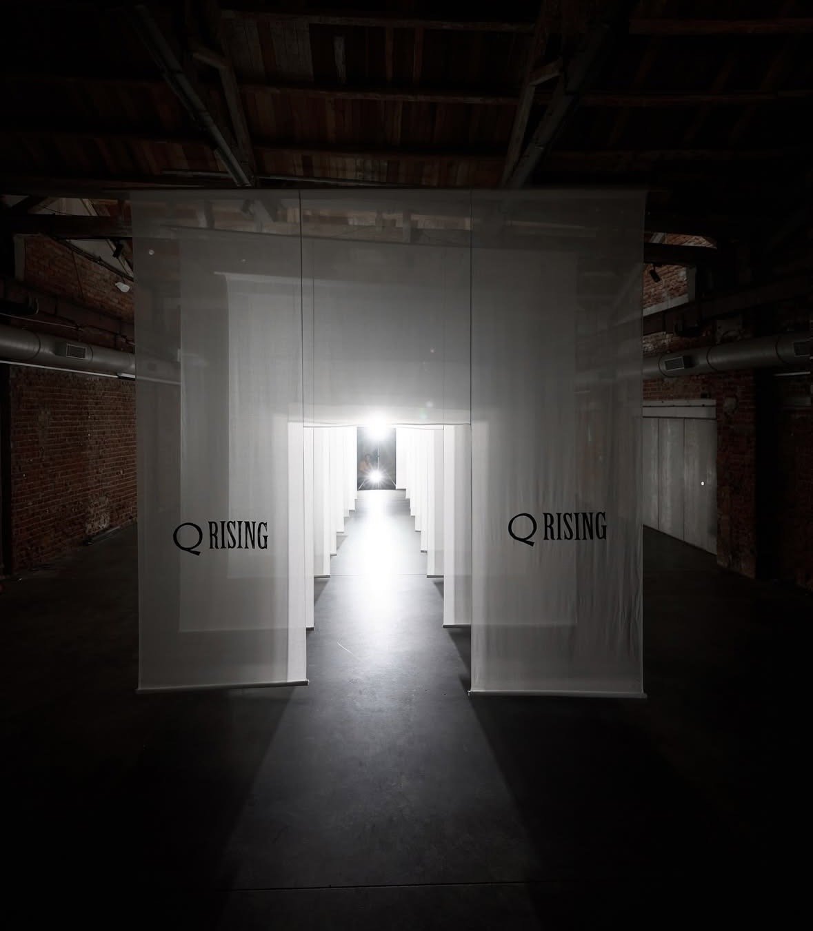 An art installation with a tunnel of white fabric panels and the words 'Q RISING' printed on both sides.