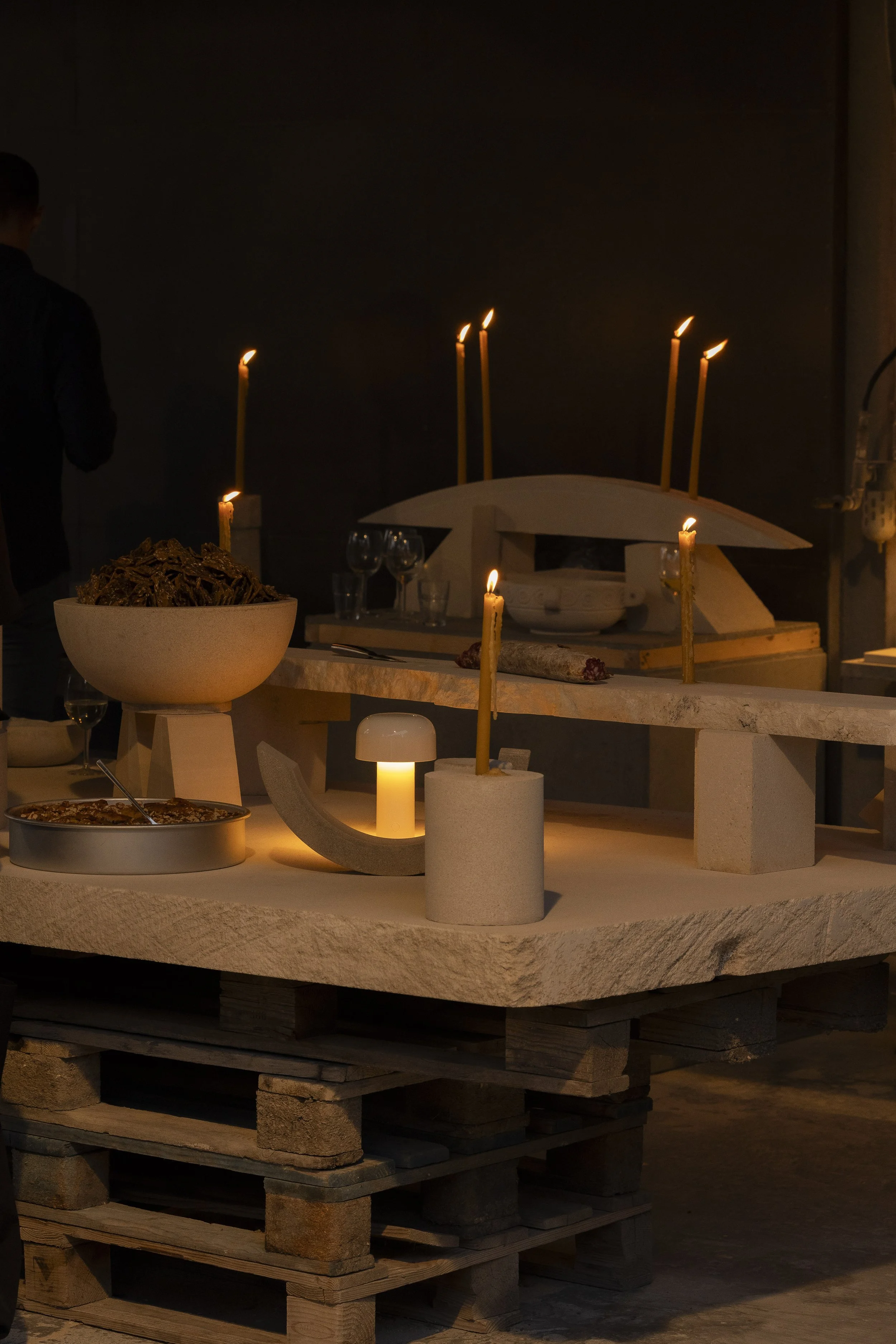A dimly lit table setup with candles, a bowl of pasta, and a pizza in a rustic setting.