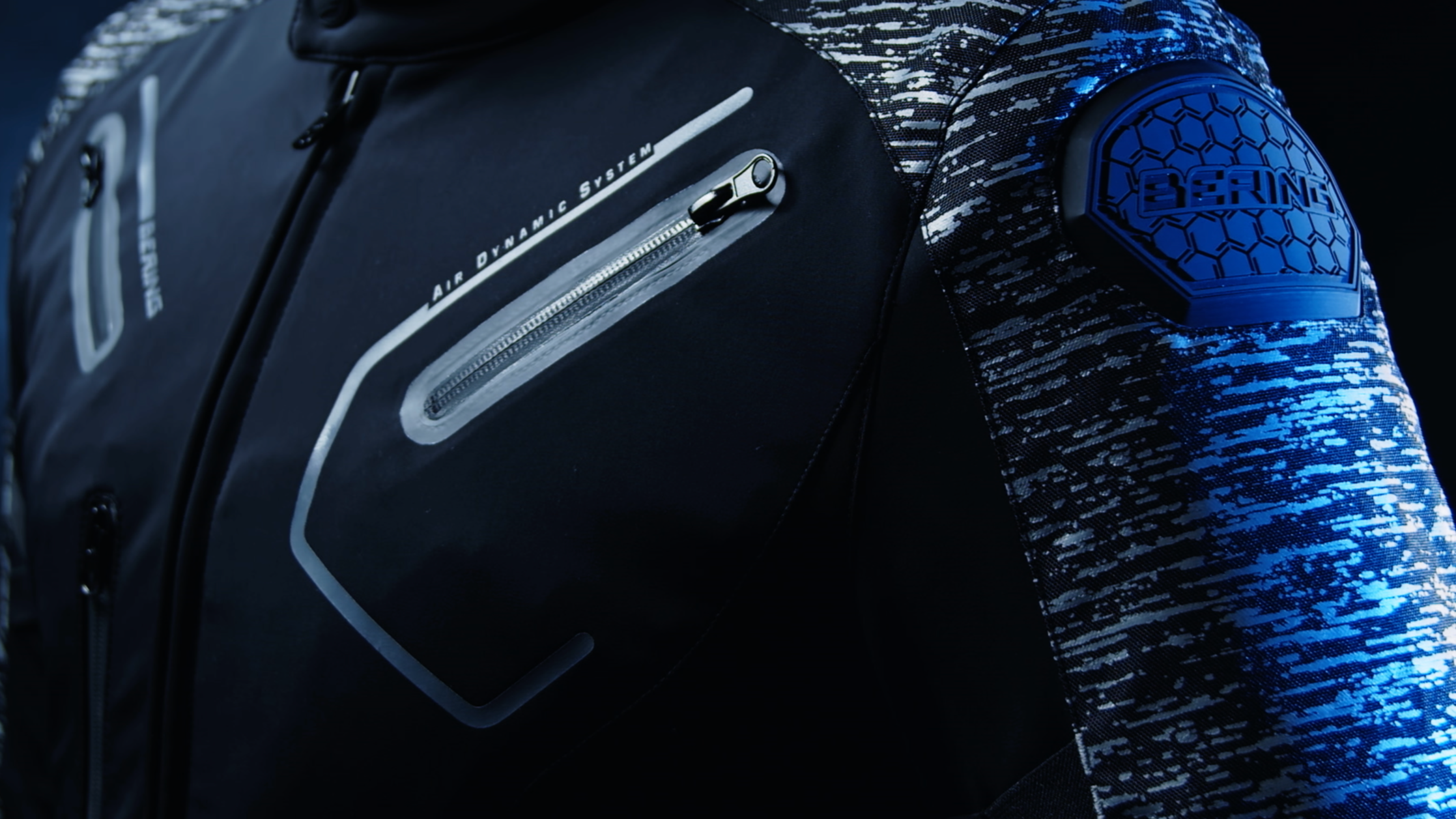 Zoom sur une veste de moto noire avec des détails argentés et un patch en caoutchouc bleu sur l'épaule.
