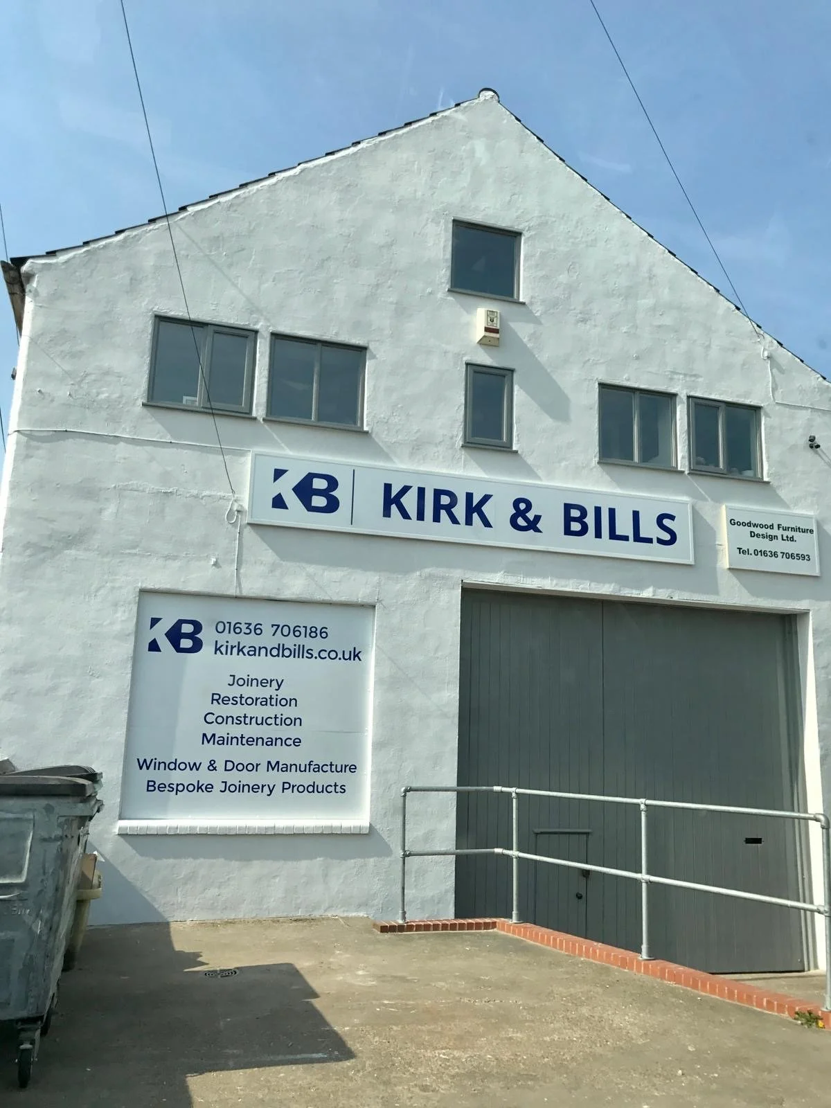 Picture showing the front of the workshop. White front, Kirk and Bills logo, blue sky.