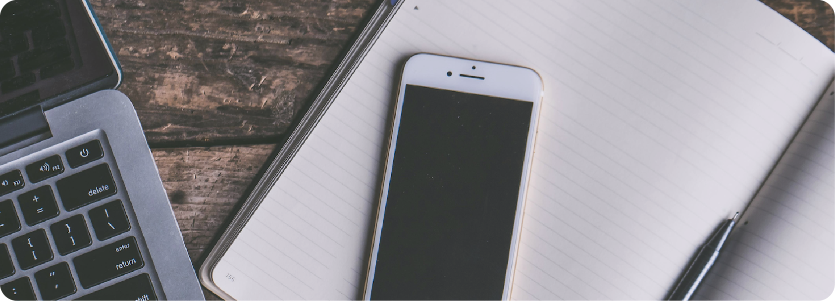 Un ordinateur portable, un téléphone intelligent, un carnet de notes et un stylo sur une surface en bois.