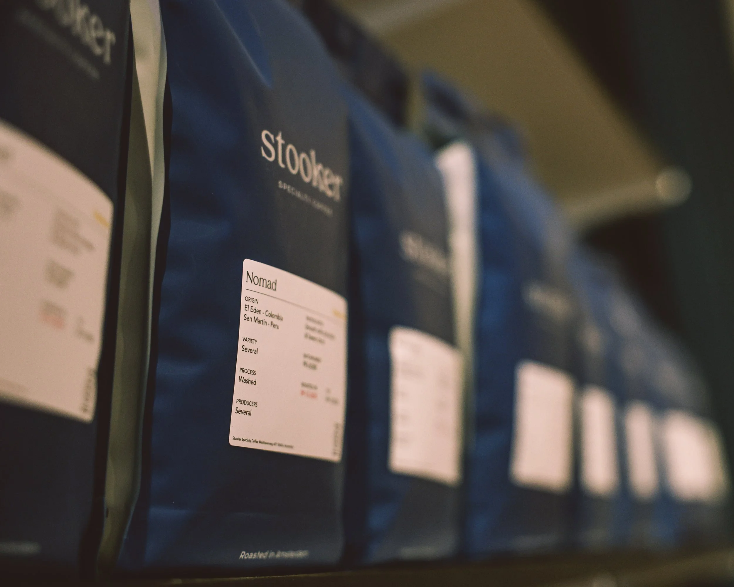 Multiple bags of Stumptown coffee on a shelf, with one prominently labeled 'Nomad', showing origin and processing details.
