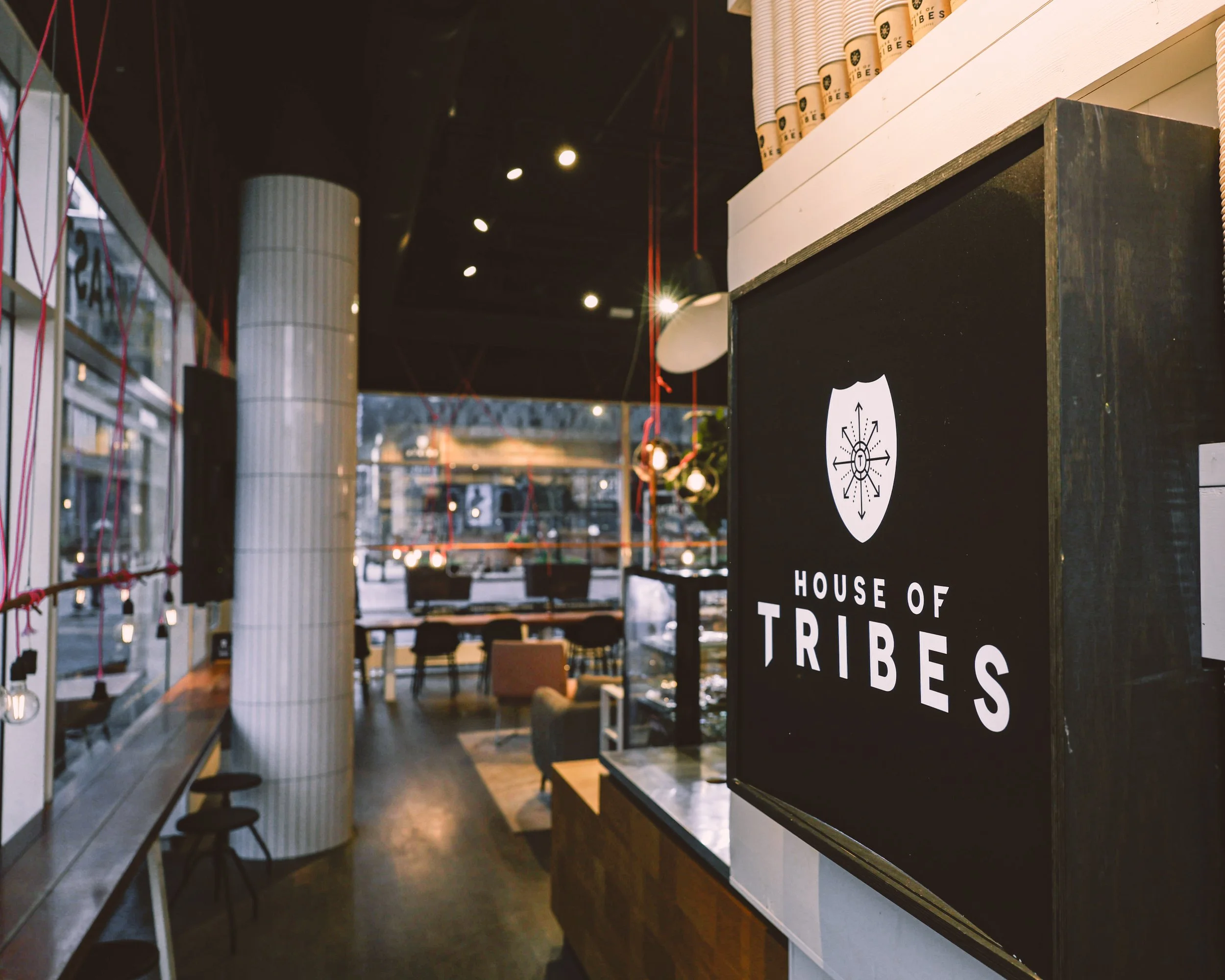 Interior of a cafe named House of Tribes with modern decor, seating area, large window, and a prominent sign displaying the name and logo.