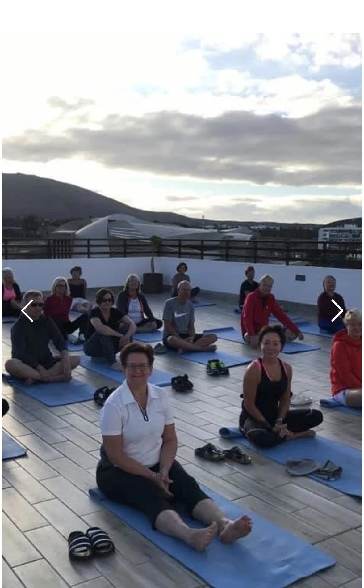 People participating in an outdoor yoga class on a rooftop terrace during sunset, sitting on blue yoga mats.