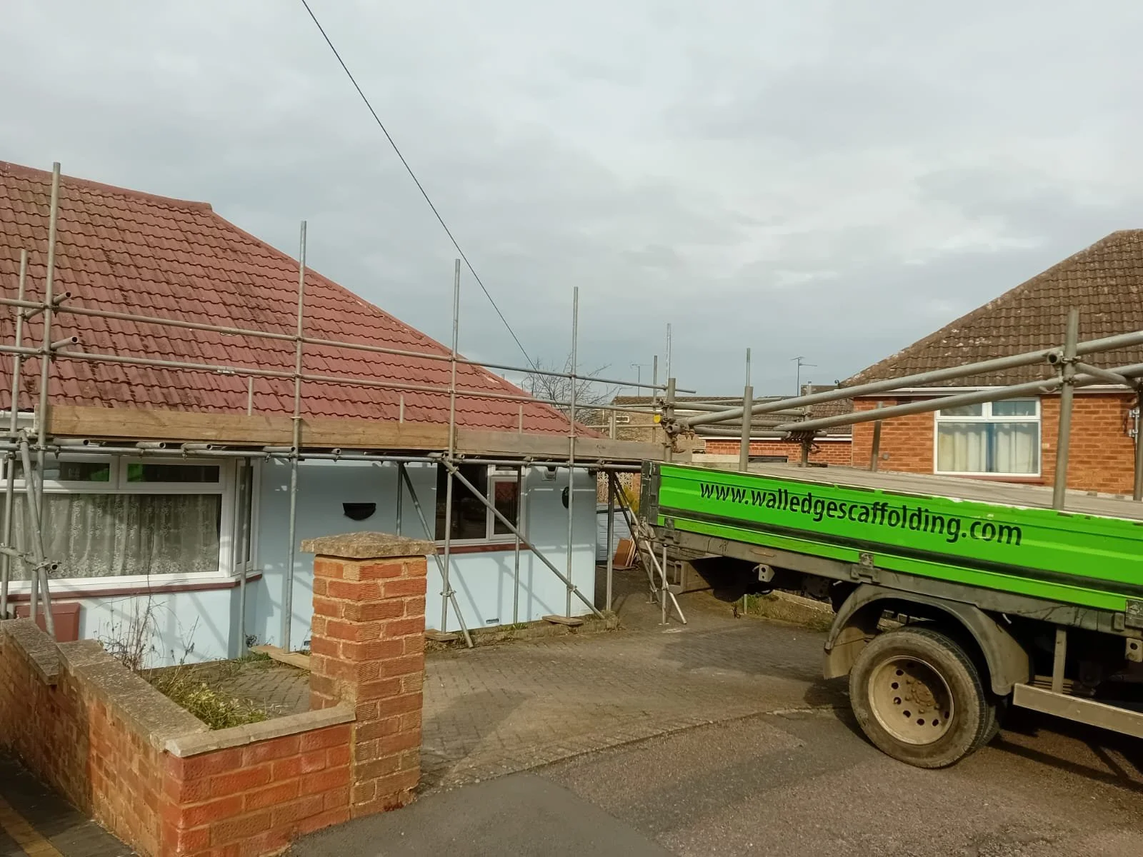 House with scaffolding and a green truck parked in front, overcast sky.