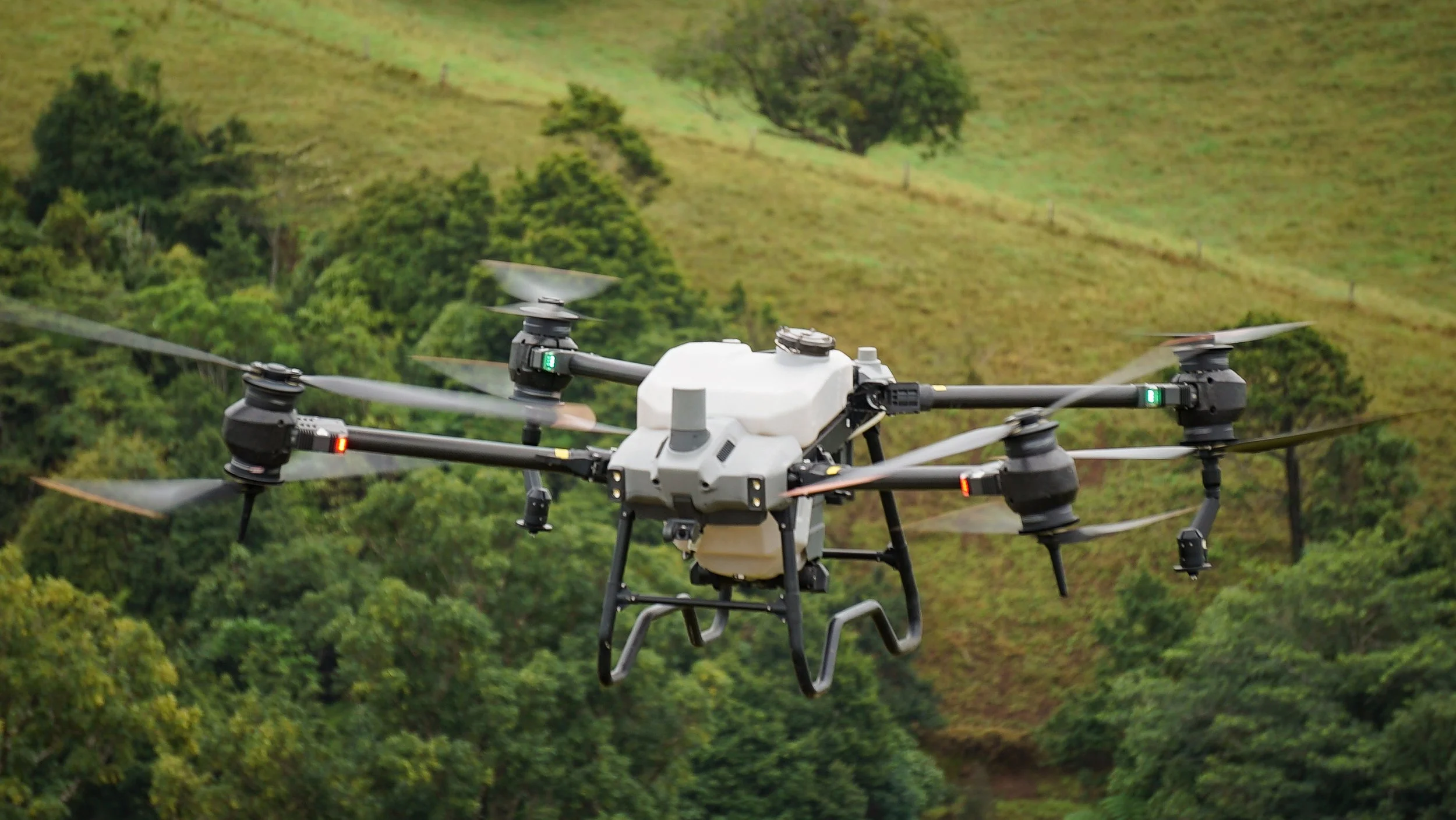 A drone flying over a green landscape with hills and trees.