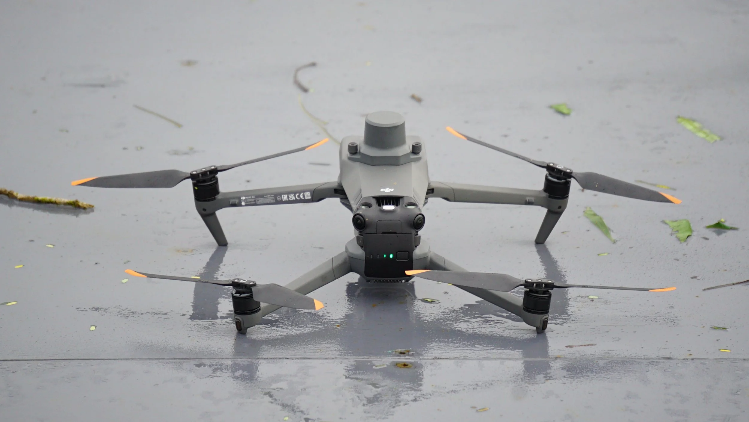 A DJI drone with four rotors is flying on a wet surface with scattered leaves.
