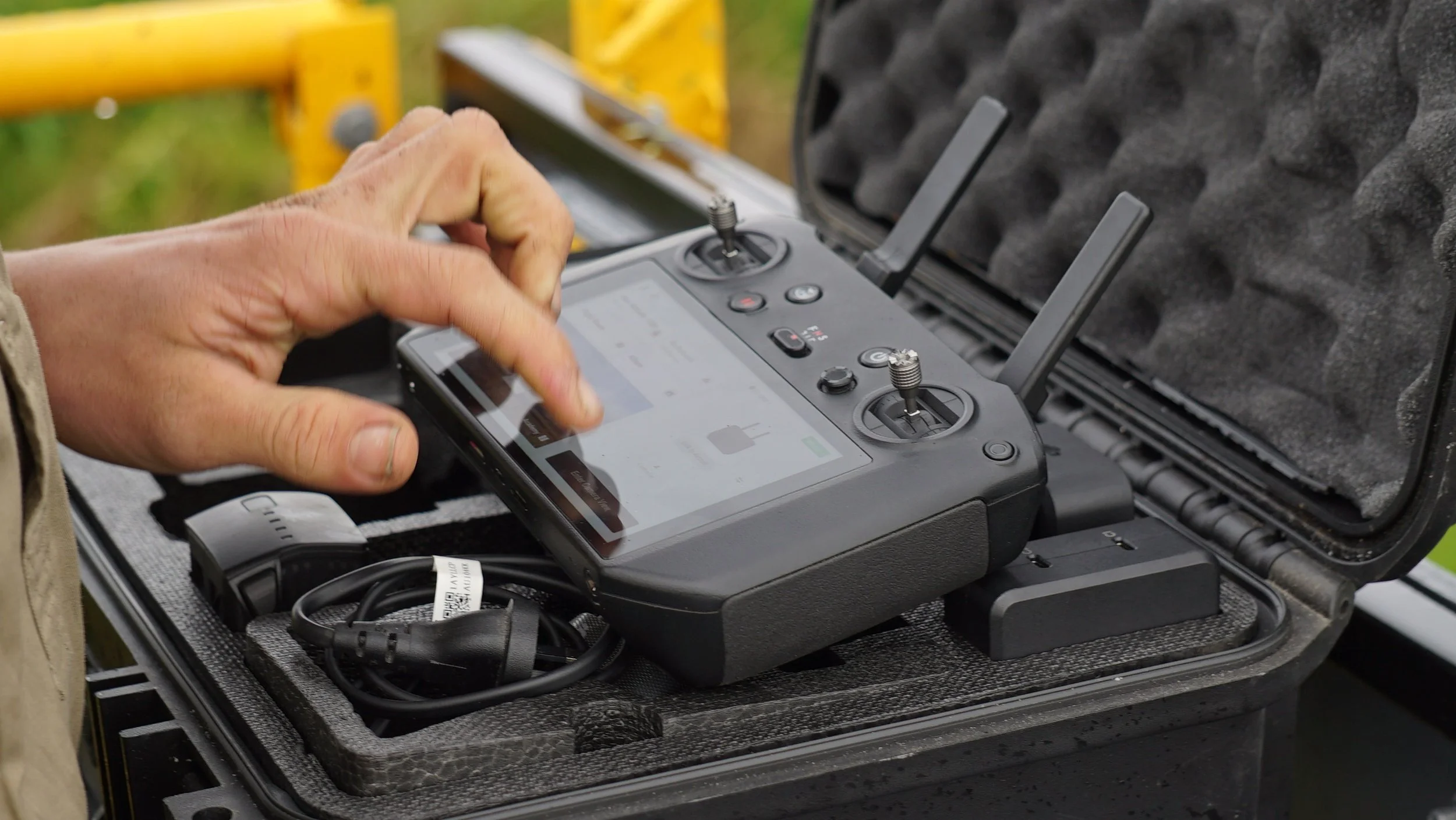 Person holding a remote control device outdoors with a foam-lined case and electronic equipment.