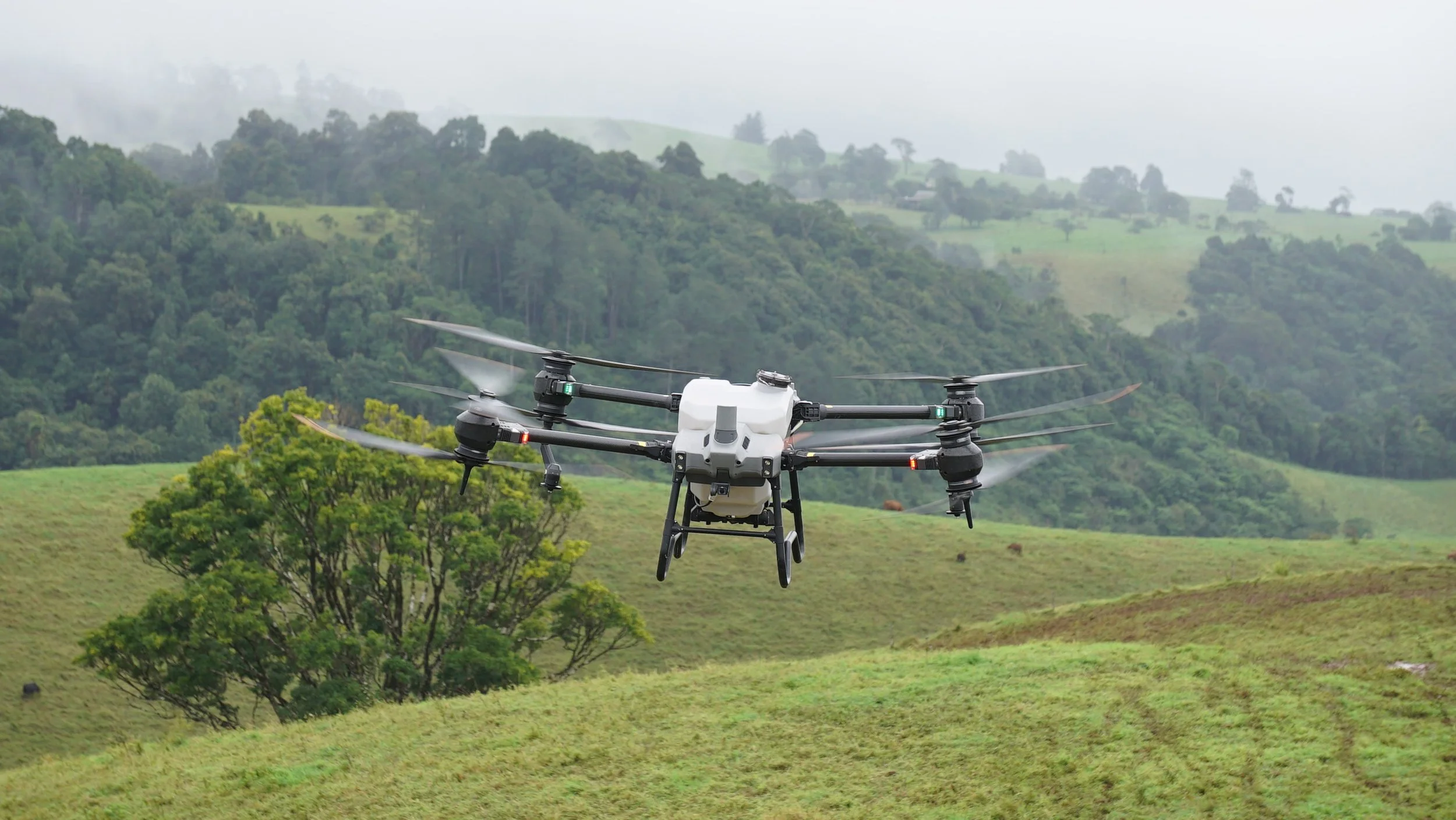 A drone flying over a green countryside landscape with trees and rolling hills.