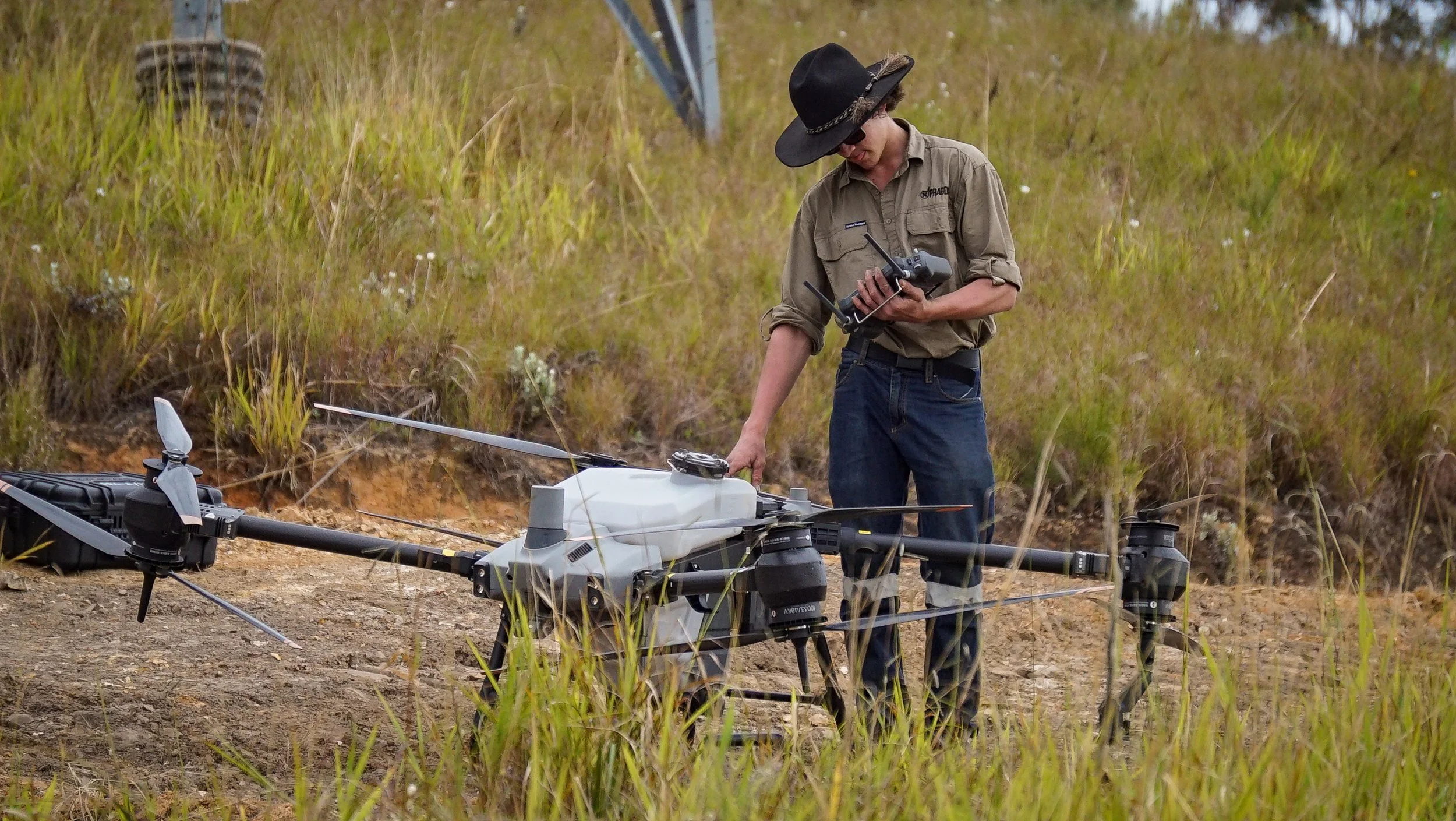 A person wearing a black hat and sunglasses operating a drone in a grassy outdoor area.