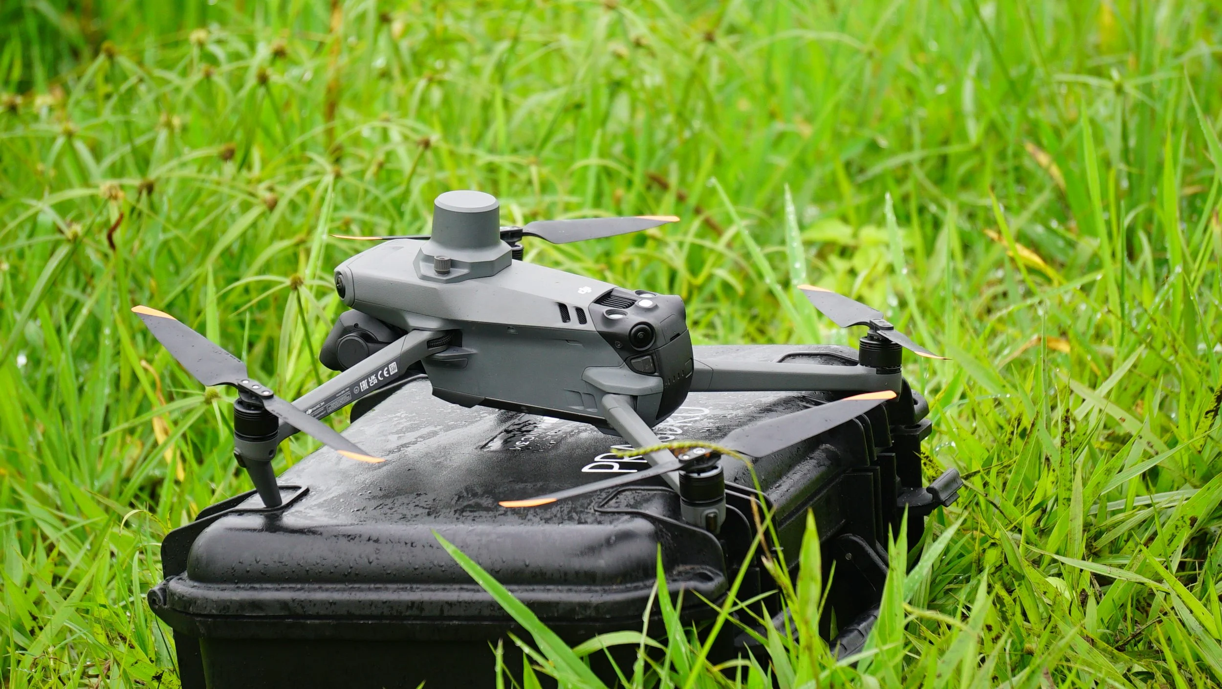 A DJI drone on top of a black case in tall green grass.