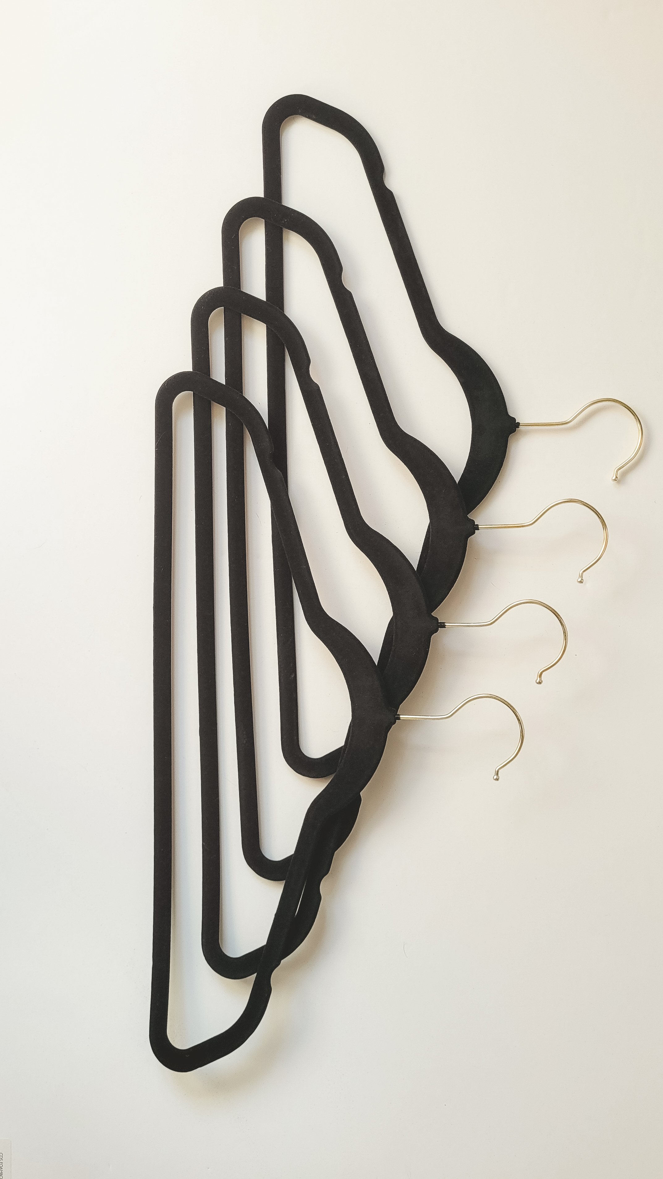 Four black velvet hangers with gold hooks stacked together on a white surface.