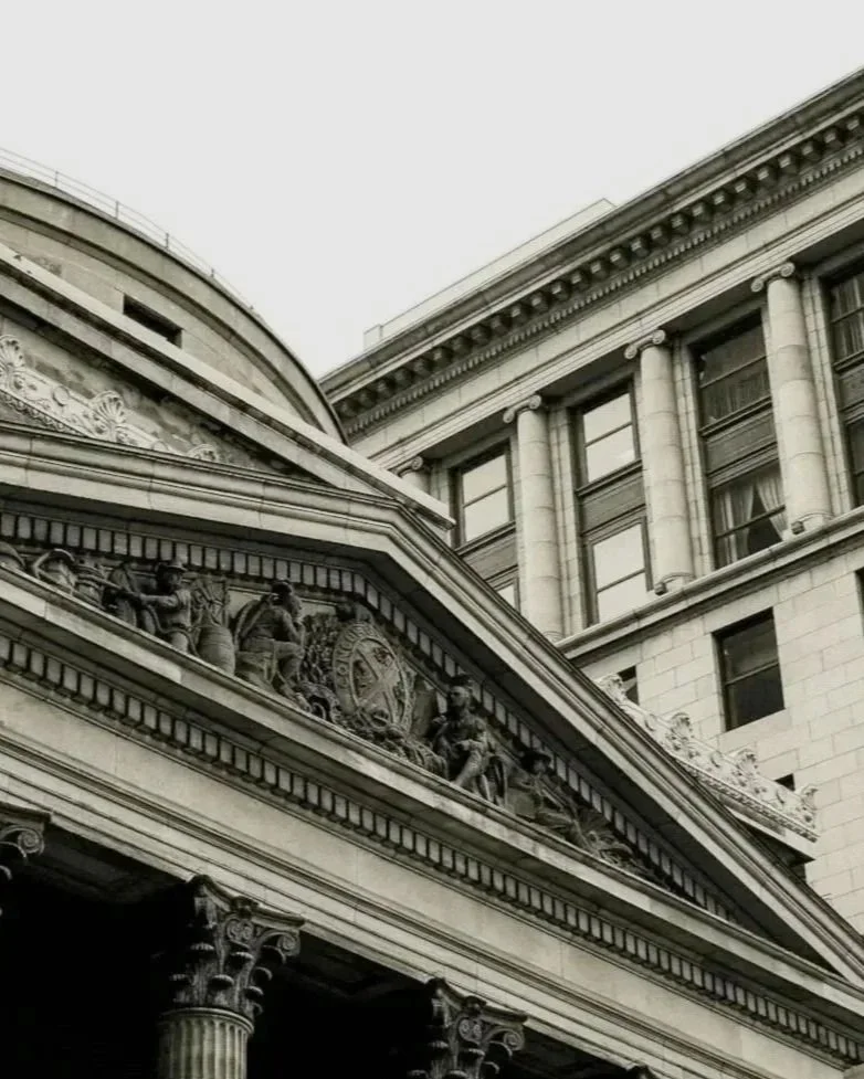 Close-up of a historic building with ornate architectural details, including columns, decorative friezes, and sculptures, in black and white.