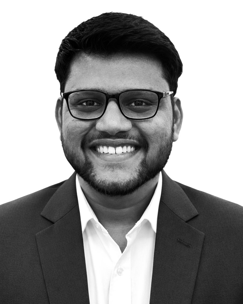 A smiling man with glasses, a beard, wearing a suit and white shirt, in a black-and-white photo.