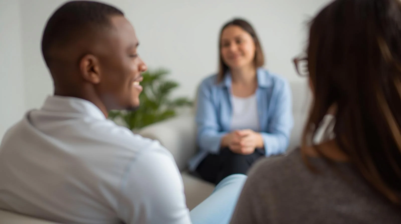 A group therapy session with four women, one smiling and three listening, in a bright room.