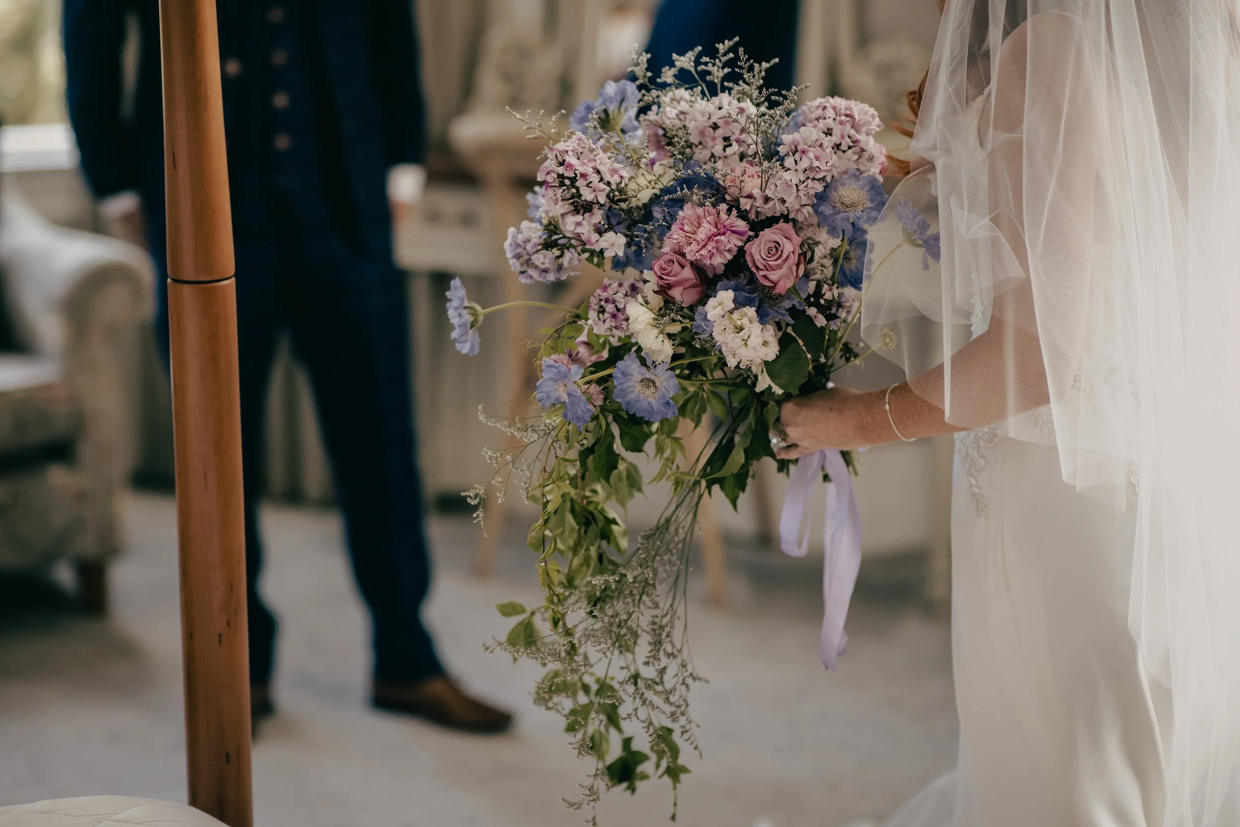 A bride holding a large bouquet of pink, purple, and white flowers during a wedding ceremony.