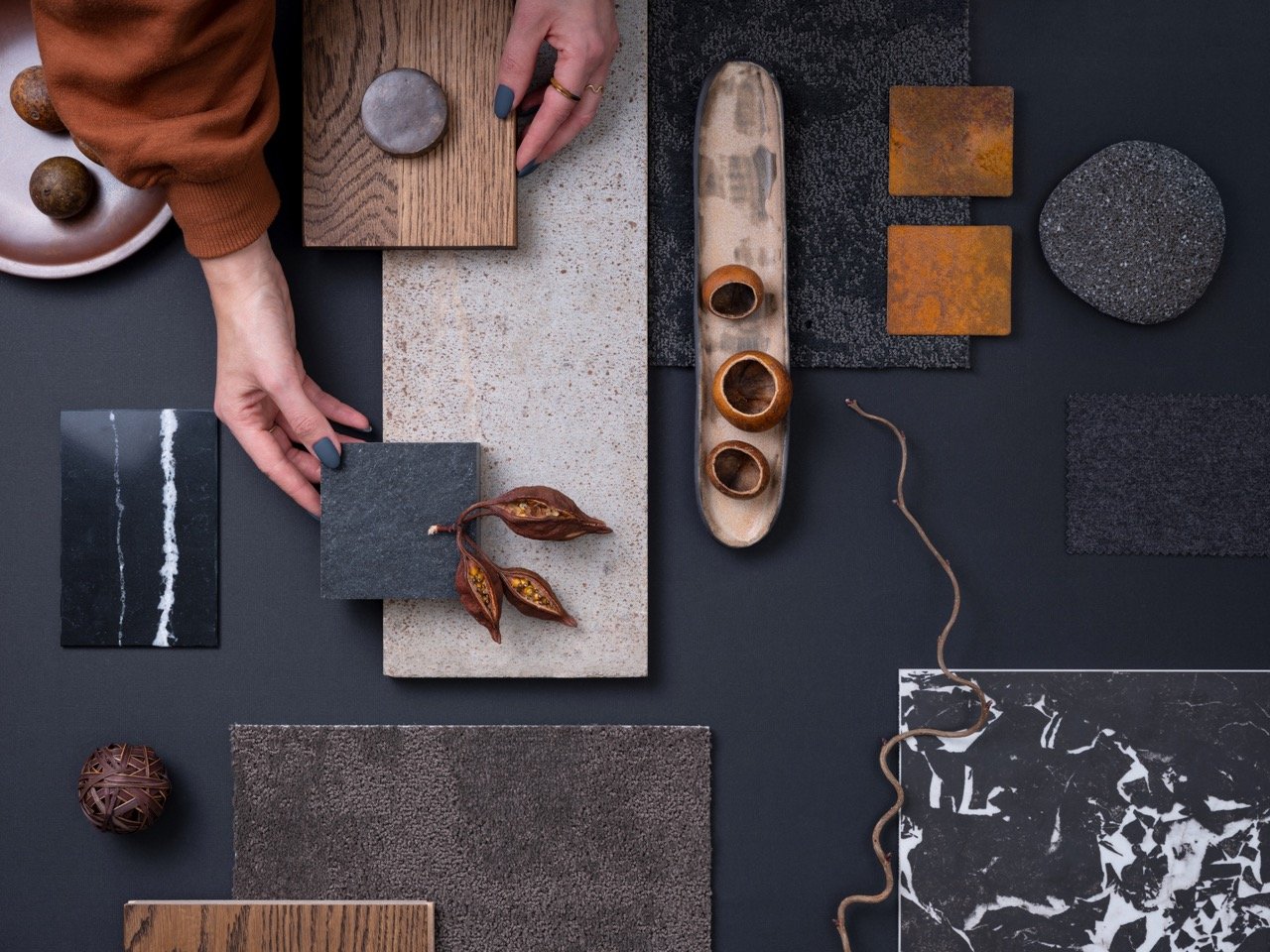 A person arranging various stone, wood, and ceramic tiles on a dark surface for a design project.