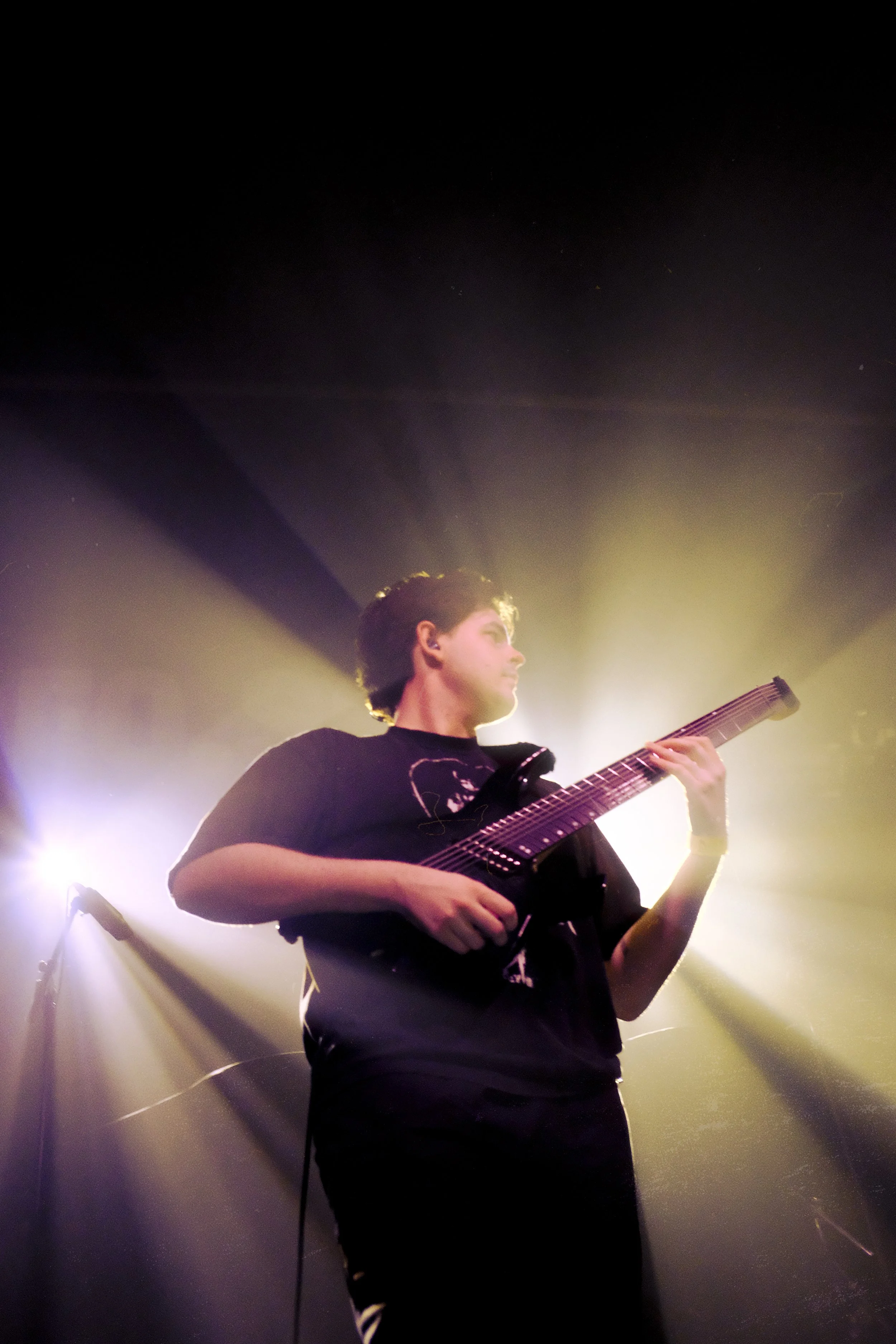 A young man playing an electric guitar on stage with bright backlighting creating a silhouette effect.