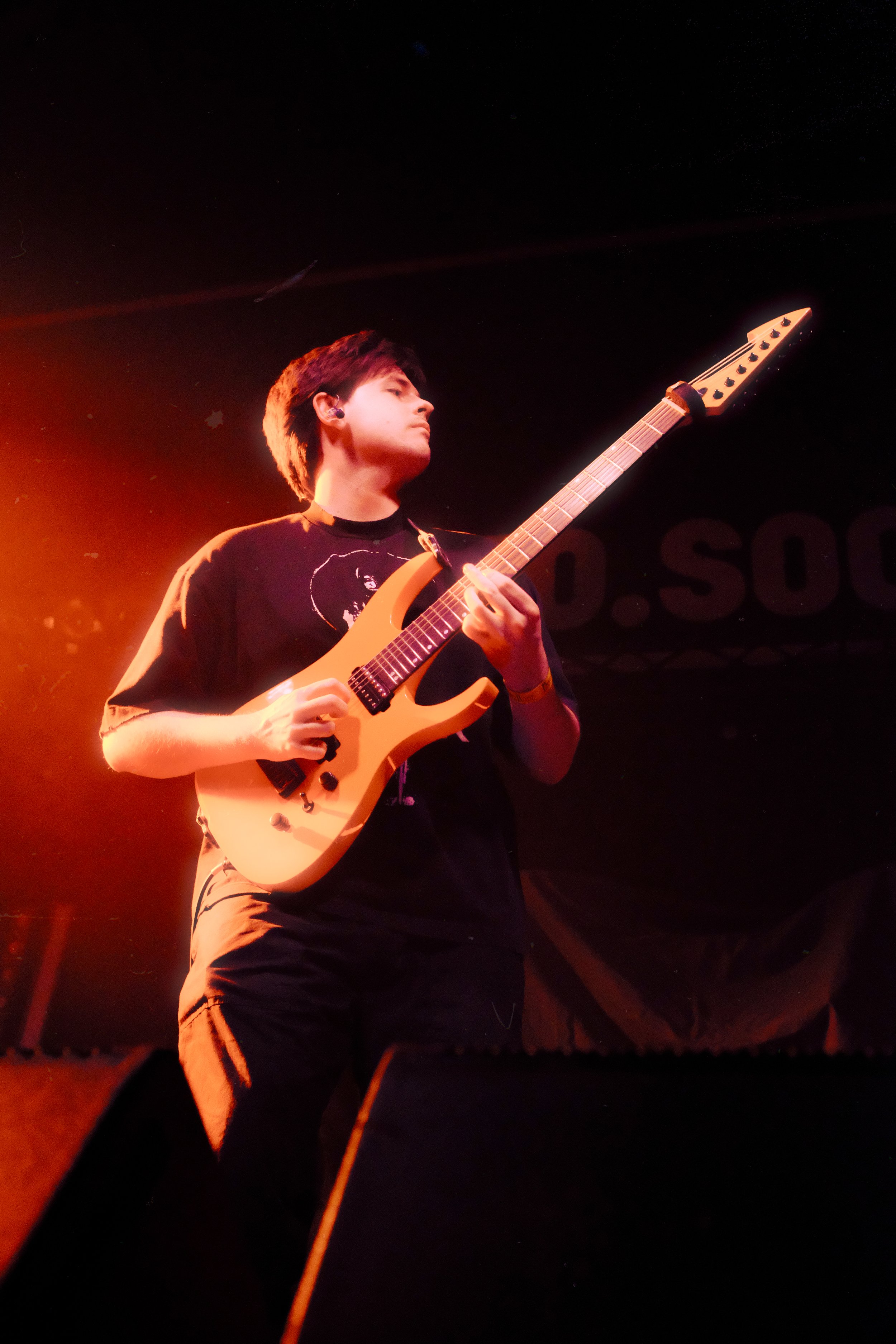 A young man playing an orange electric guitar on stage under red lighting.