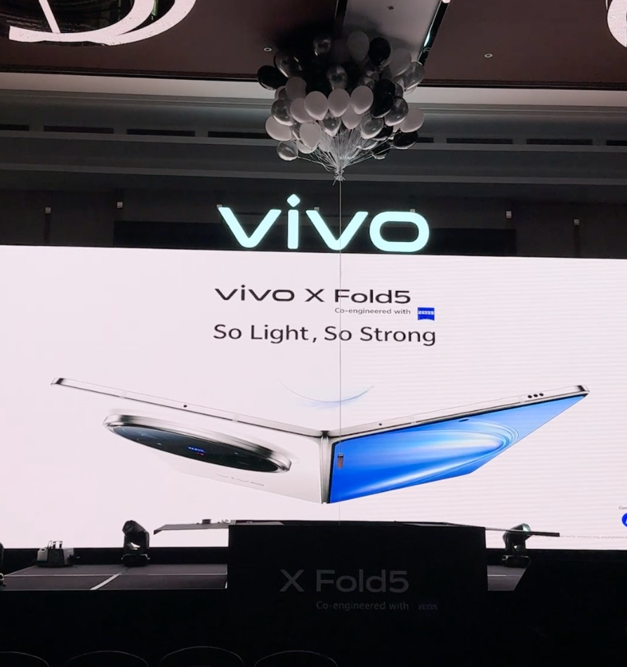 Large screen display showcasing the Vivo X Fold5 smartphone with the slogan "So Light, So Strong." The display includes an image of the foldable phone and the Vivo logo at the top. Black and white balloons are hanging from the ceiling.