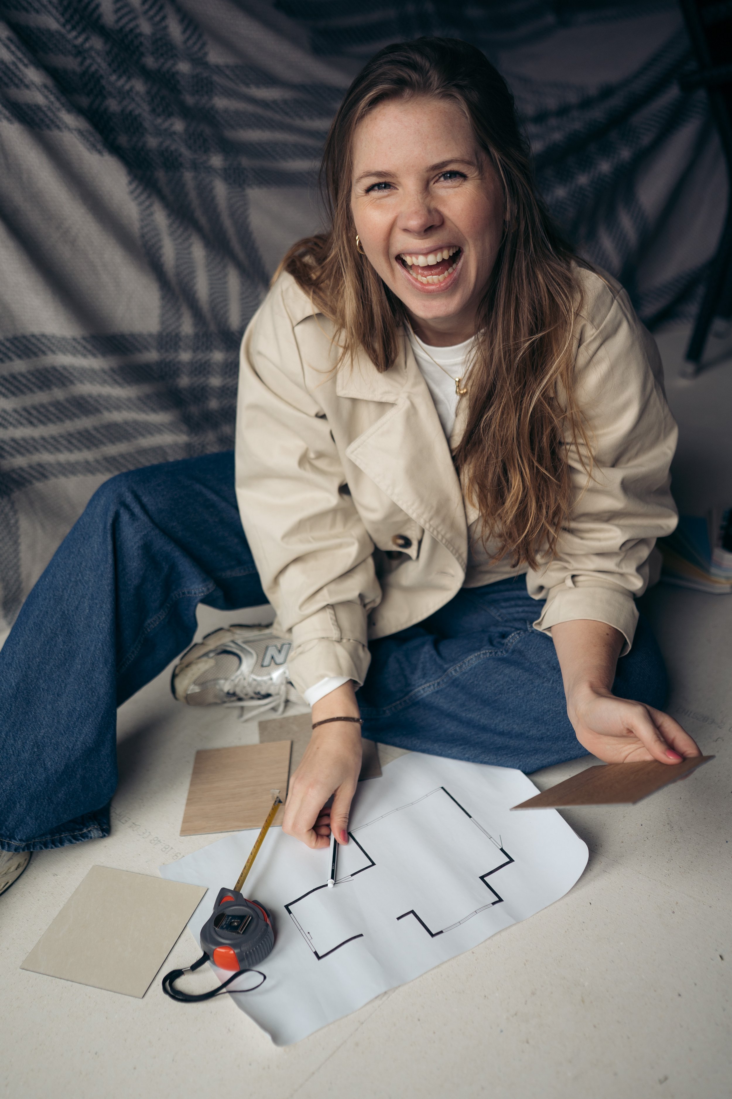 Vrouw die aan een plattegrond en kleurenkaarten werkt, zittend op de vloer met meetlint en meetapparatuur.