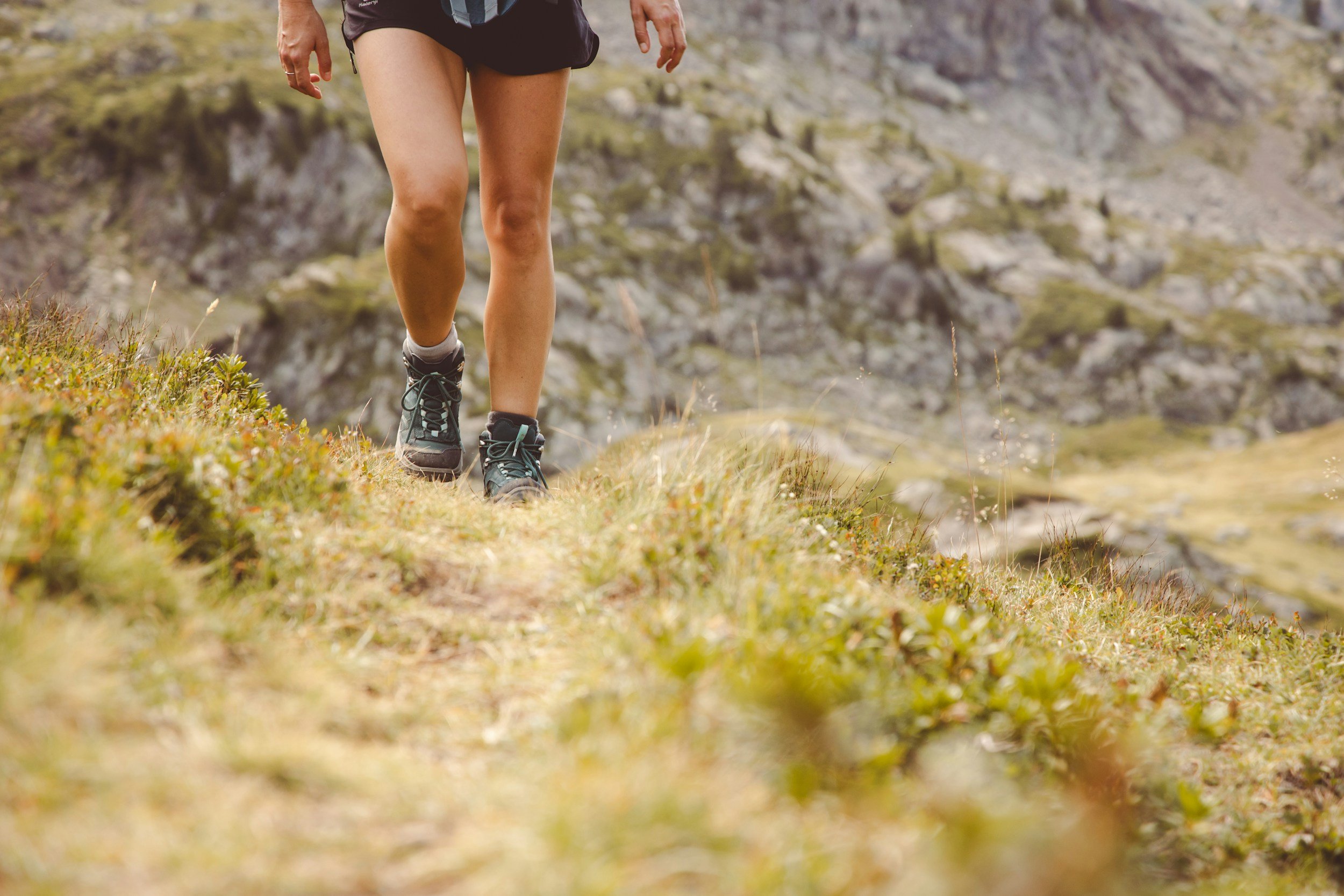 A person running on a grassy trail in a hilly area, only their legs and shoes are visible.
