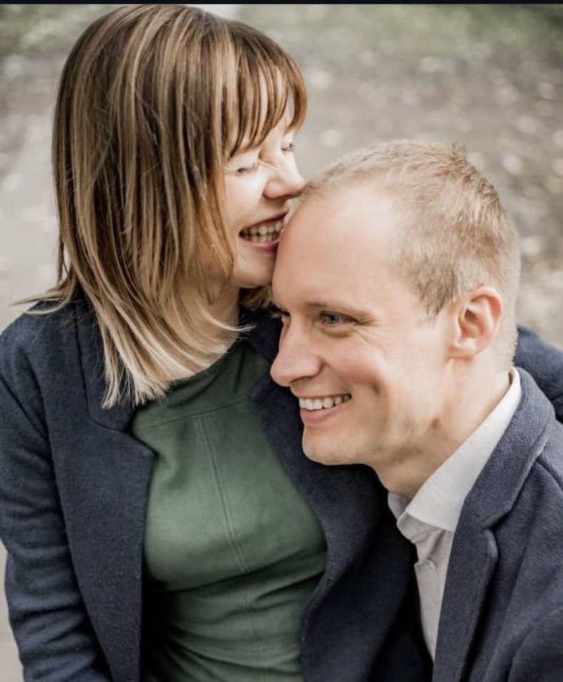 Ein lachendes Paar, die Frau küsst den Mann auf die Wange, im Freien.