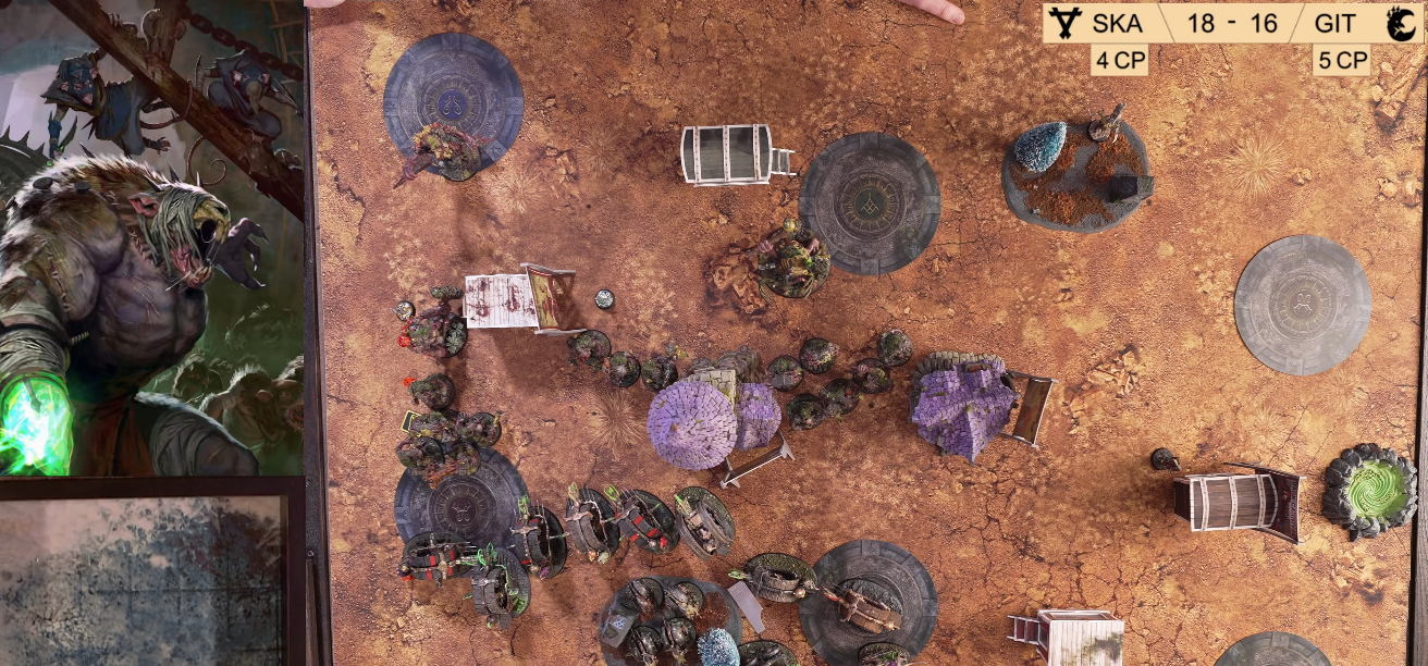 Gameplay of a tabletop miniature game on a dusty, planet-like surface with various game pieces, tokens, and terrain elements.