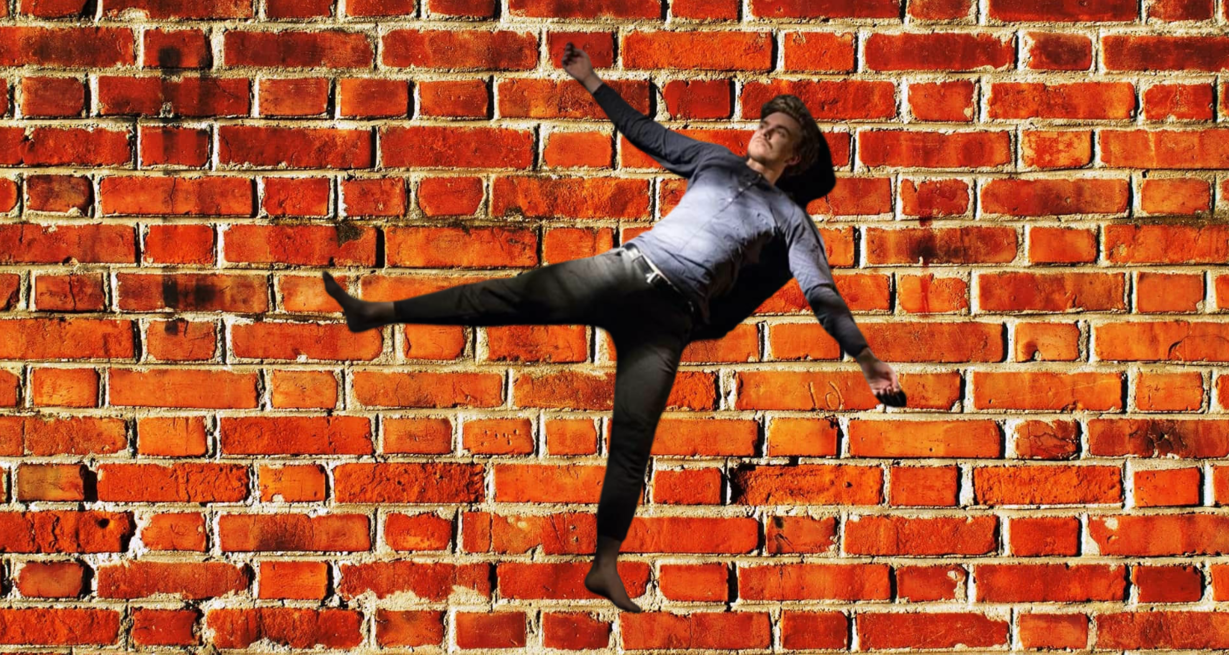 A man in business attire is seen mid-fall against a red brick wall background, with one arm reaching upward and one leg extended sideways.