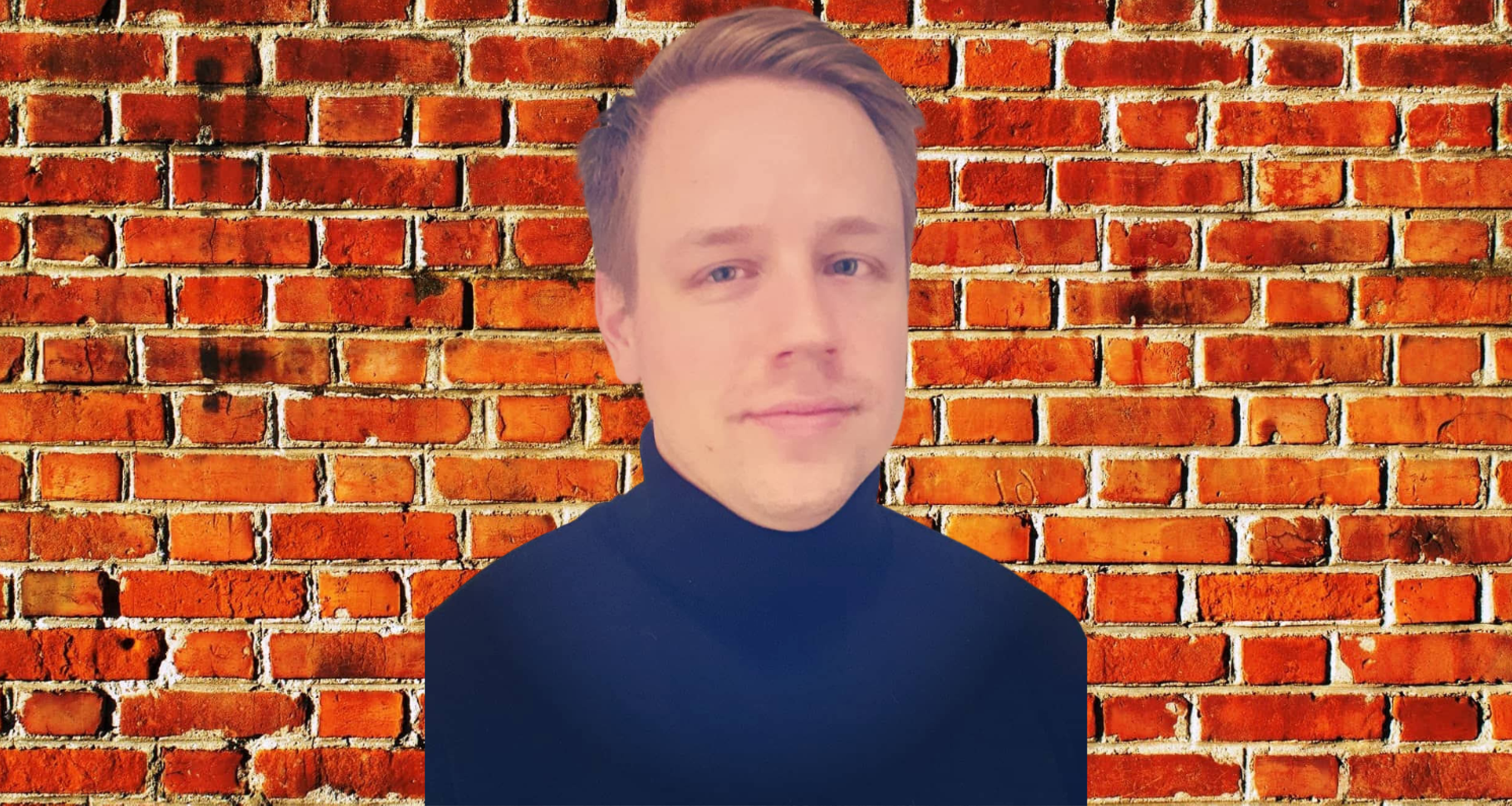 A person with short, light brown hair and a fair complexion, wearing a black turtleneck sweater, standing in front of a brick wall.
