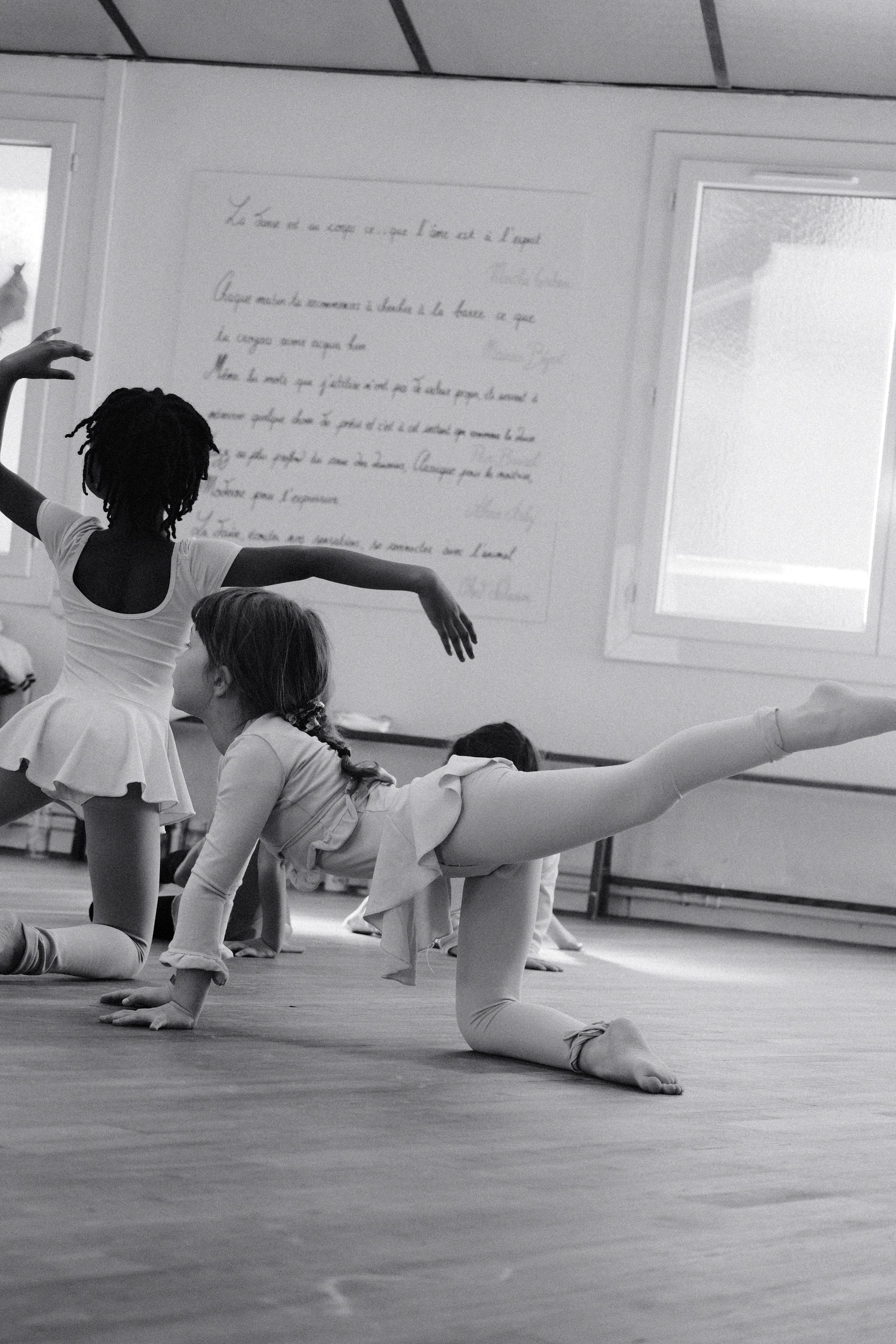 Deux jeunes filles en ballet pratiquant une pose de danse classique dans un studio en noir et blanc.