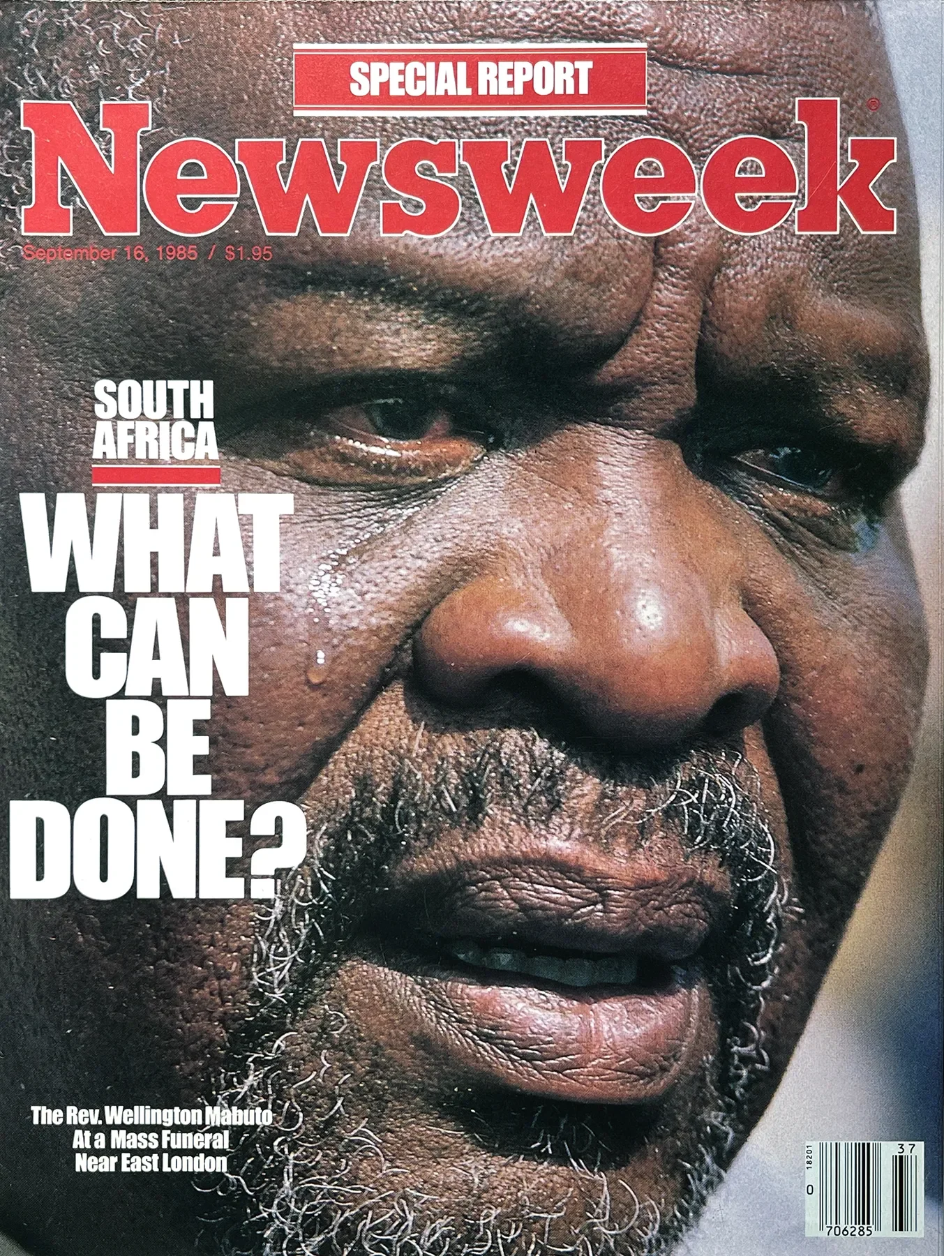 Close-up photo of an elderly man's face with dark skin and gray facial hair, featuring the cover of Newsweek magazine from September 16, 1985, with a large red and white headline reading 'WHAT CAN BE DONE?' and smaller text mentioning the Rev. Wellington Mabuto at a mass funeral near East London.